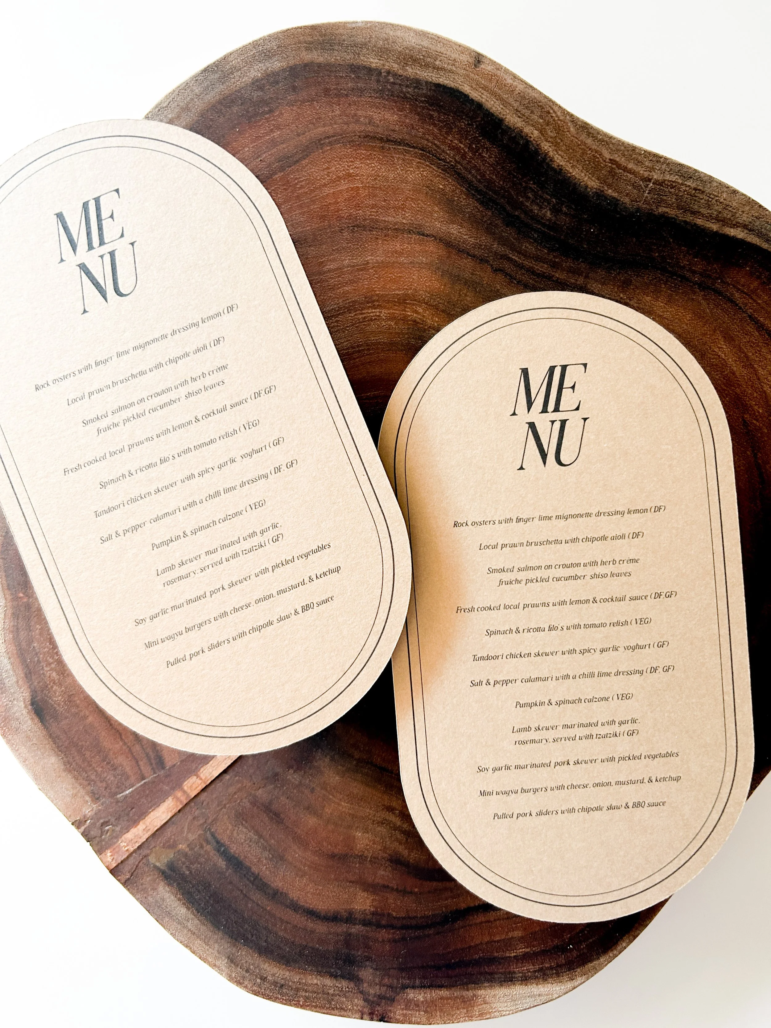 Two menus with the restaurant name 'MENÙ' on cream-colored paper, set on a round wooden tray.