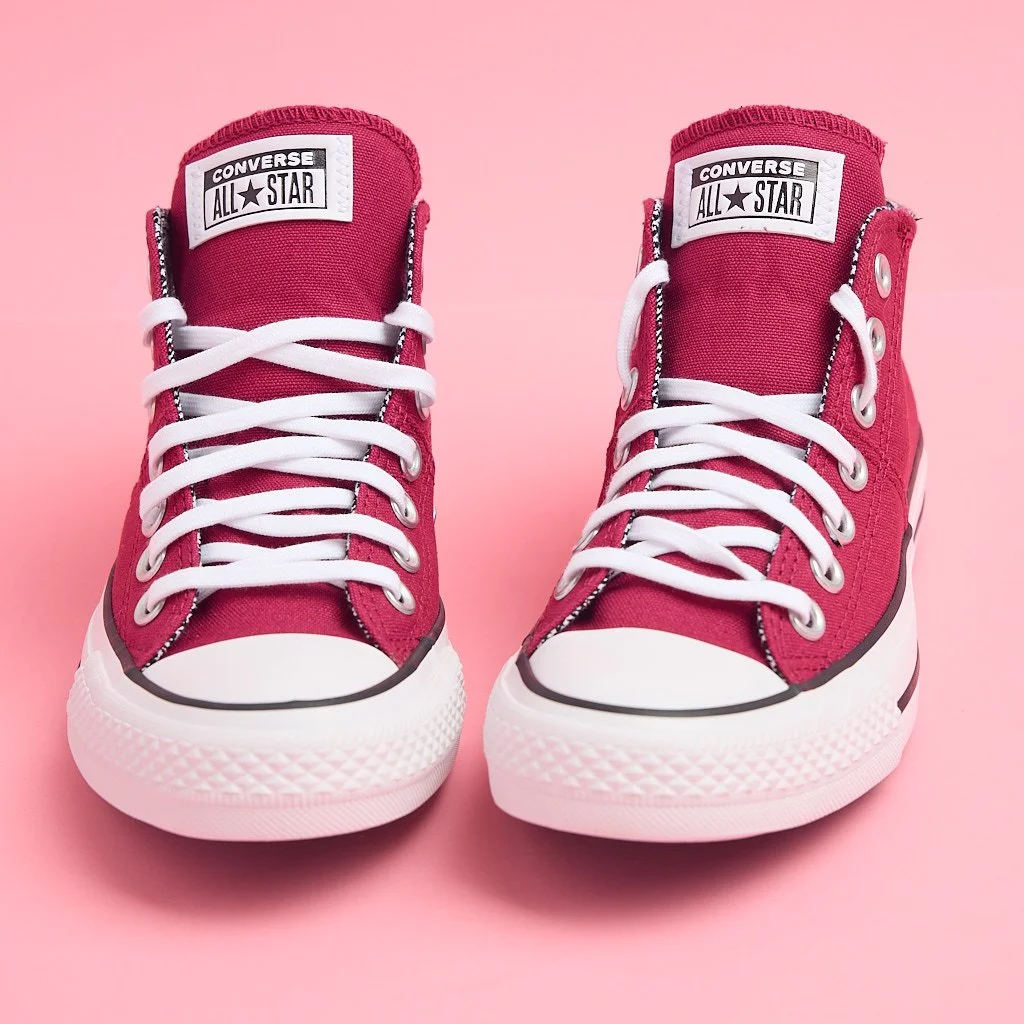 Pair of pink Converse All-Star high-top sneakers with white laces on a pink background.