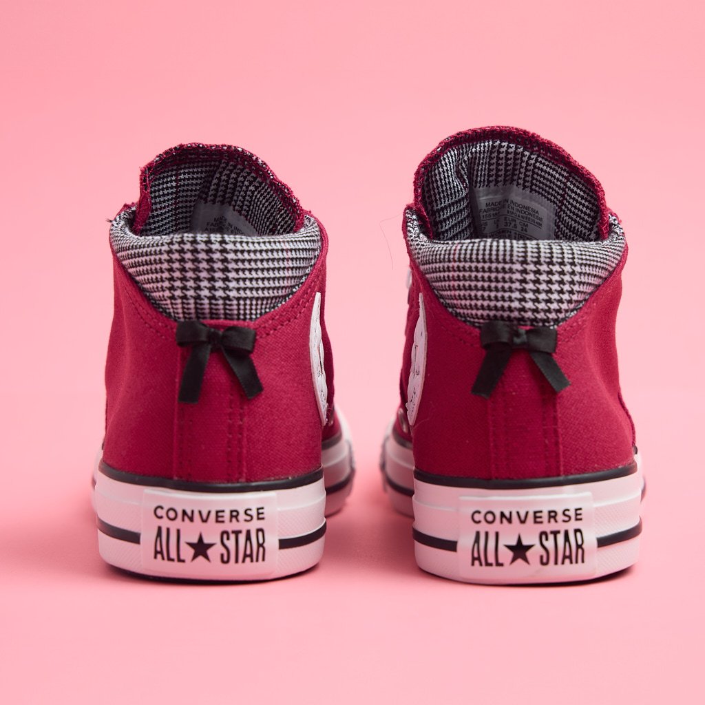 Pair of red Converse All Star high-top sneakers with black laces, white soles, and black-and-white checkered lining, positioned on a pink background.