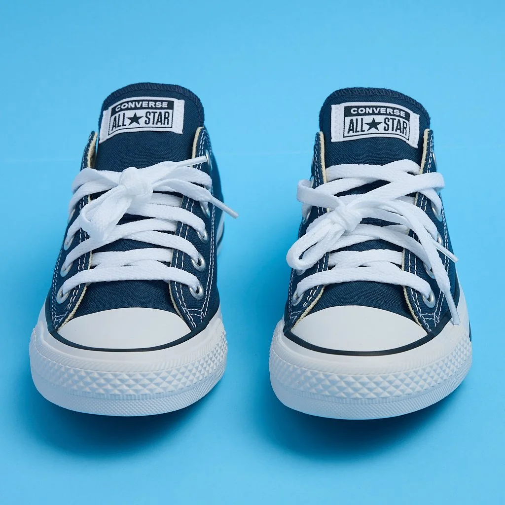 Pair of navy blue Converse All Star sneakers with white laces on a light blue background.
