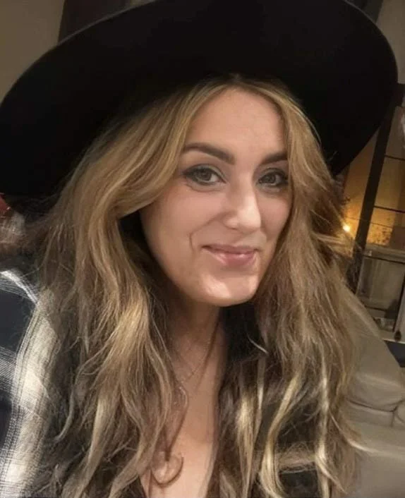 A picture of a smiling Cherie in a plaid shirt and black hat