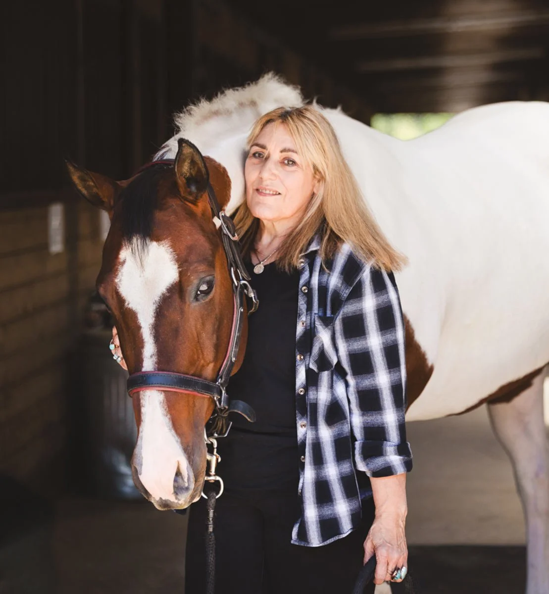 Cherie stands with a skewbald horse resting its head on her shoulder