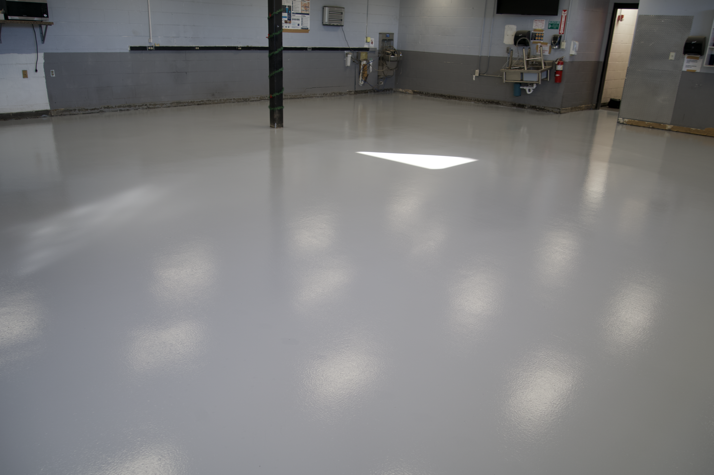 Epoxy-coated empty garage floor with gray walls and overhead lighting.