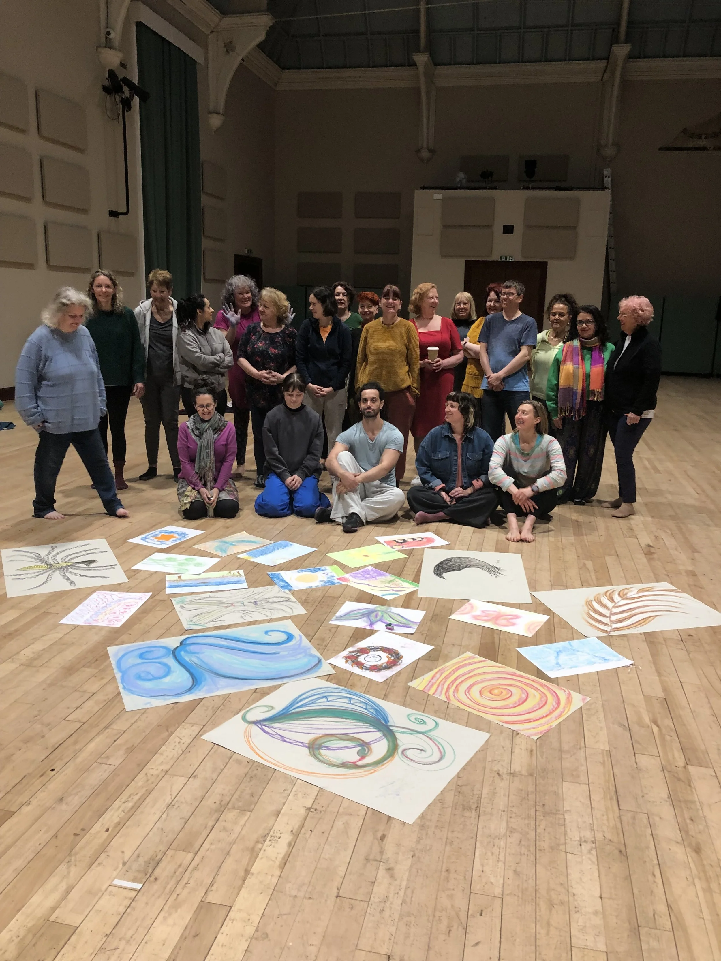 Group of people standing and sitting in an indoor studio with colorful abstract artwork laid out on the floor.