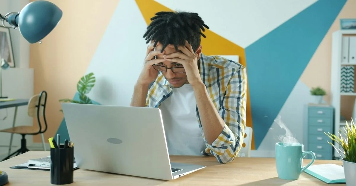 Business owner looking frustrated with hands on forehead near laptop