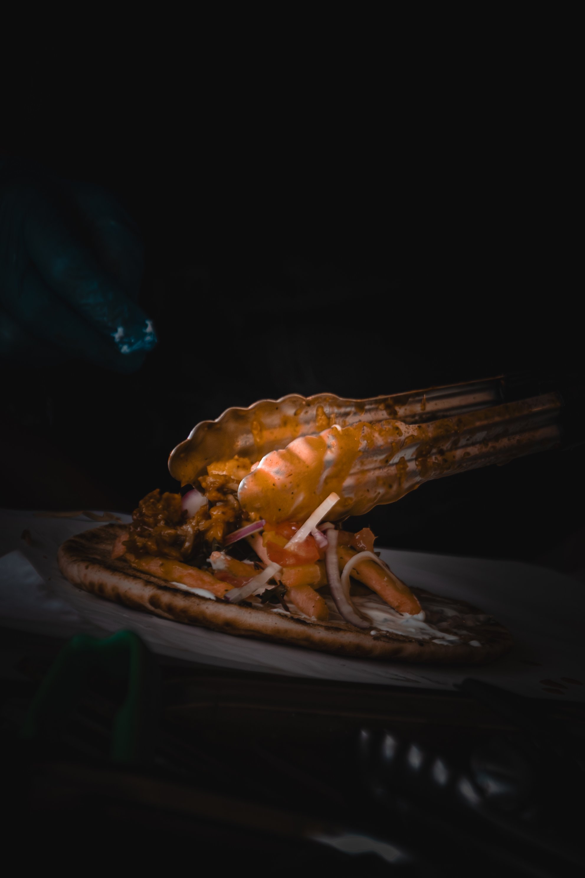 A taco shell filled with shredded meat, onions, and sauce, being held with tongs.