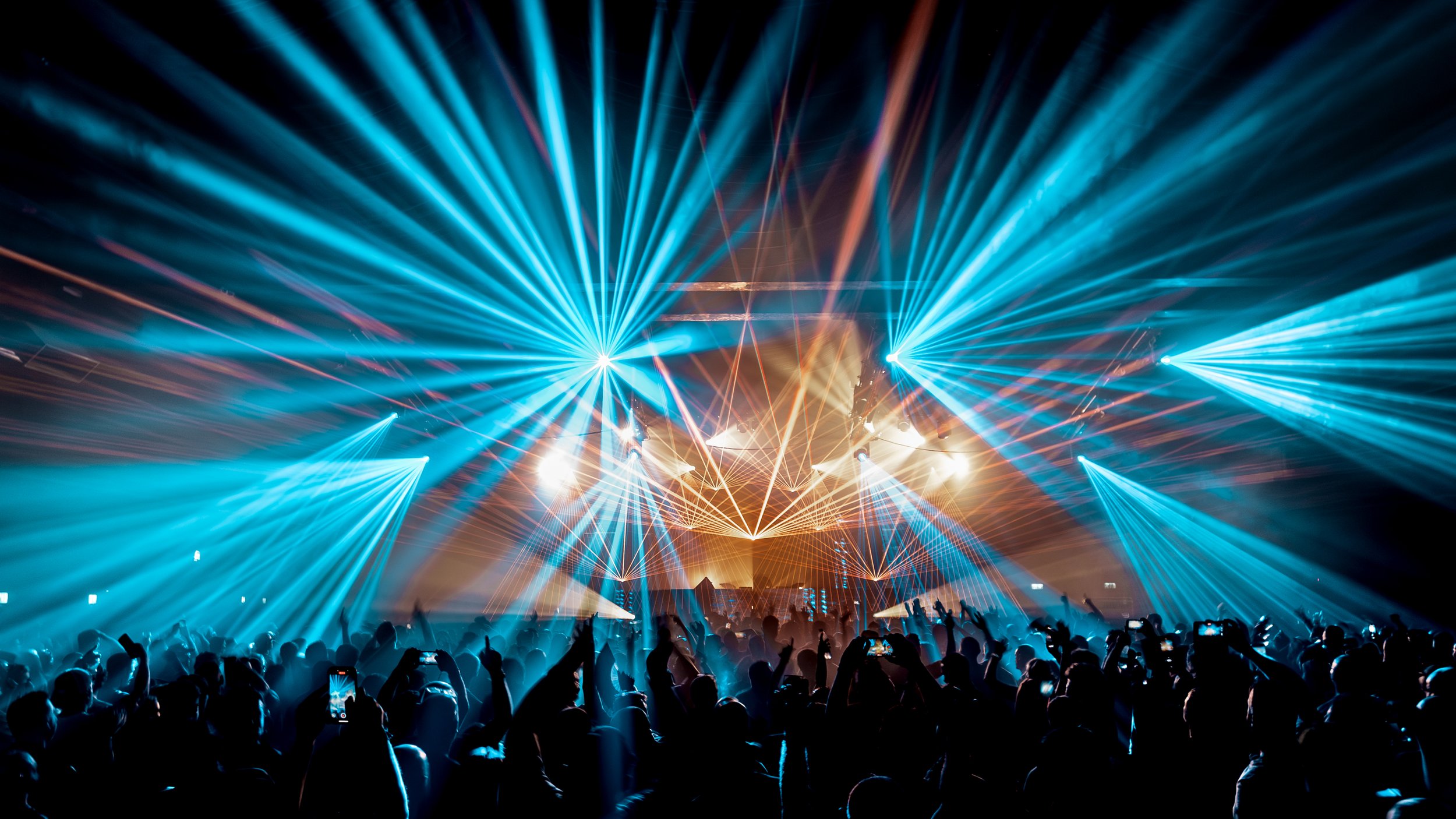 Concert or music festival with blue and orange laser lights and a crowd of people taking photos.