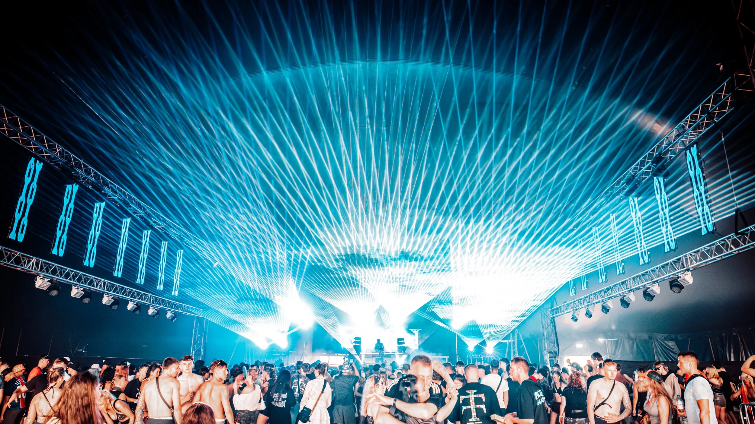 Crowd at a concert or music festival with bright blue laser lights crisscrossing overhead.