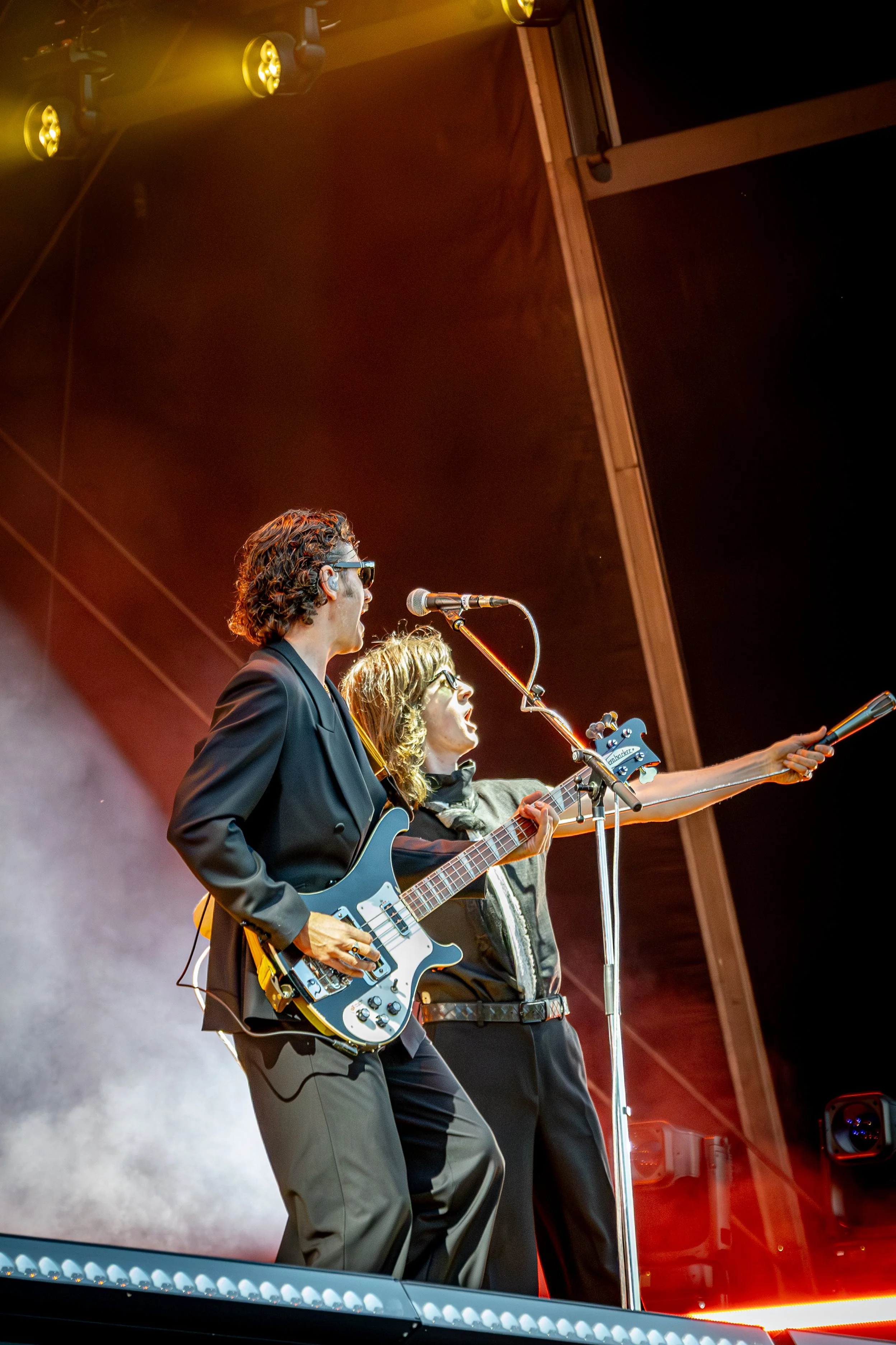Musicians performing on stage, one playing guitar and another singing into a microphone, under stage lighting.