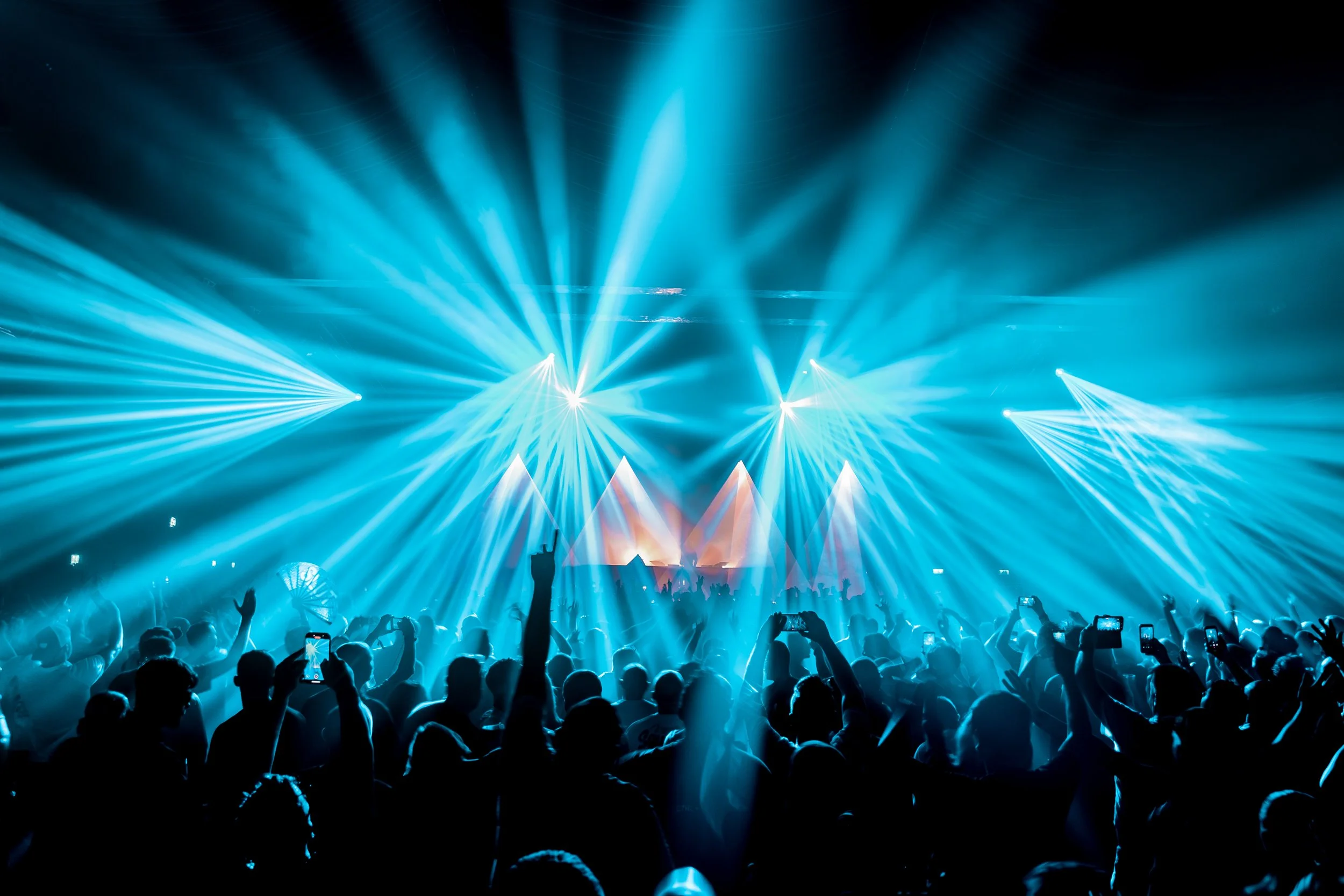 Crowd at a concert with blue stage lights and laser show.