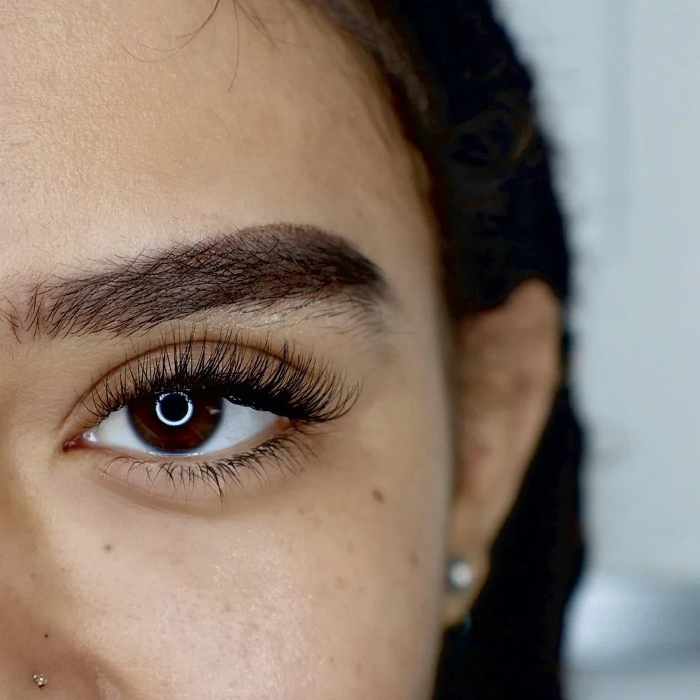 Close-up of a person's face focusing on the left eye, with well-groomed eyebrows, long eyelashes, and smooth skin, showcasing eye makeup and earrings.