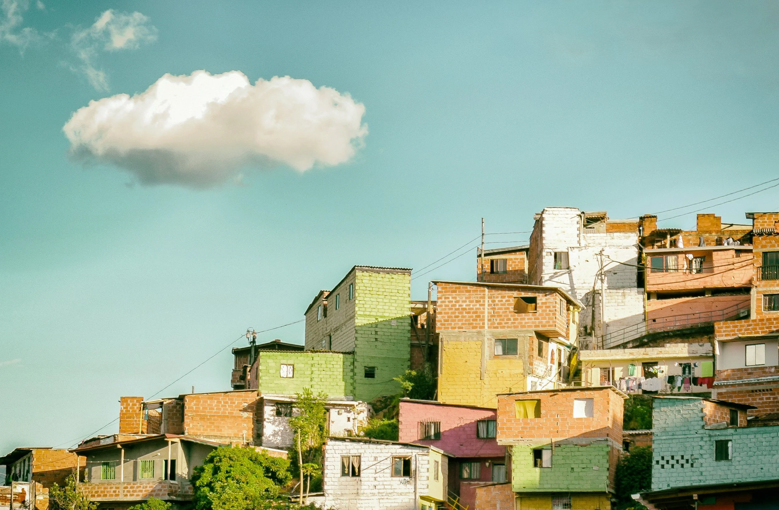 Habitat improvisé avec maisons en briques et en ciment coloré sur une colline, sous un ciel bleu avec nuage blanc.