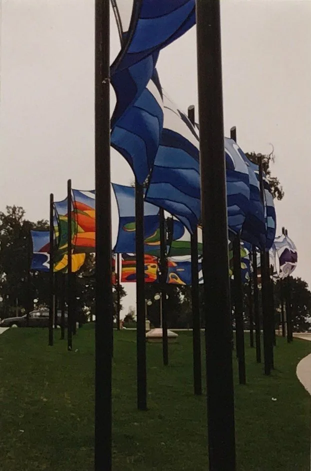 Multiple colorful abstract flags mounted on black poles on a grassy area outdoors. NCC banner competition winner Jane Thompson, 1988 Ottawa Ontario Canada.