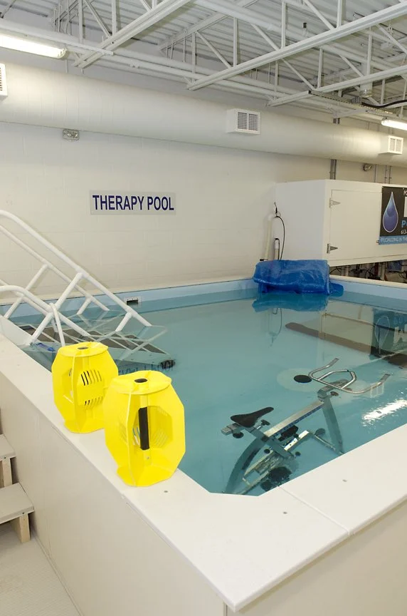 Indoor therapy pool labeled 'THERAPY POOL' with yellow water exercise equipment, stairs, and a blue cover.