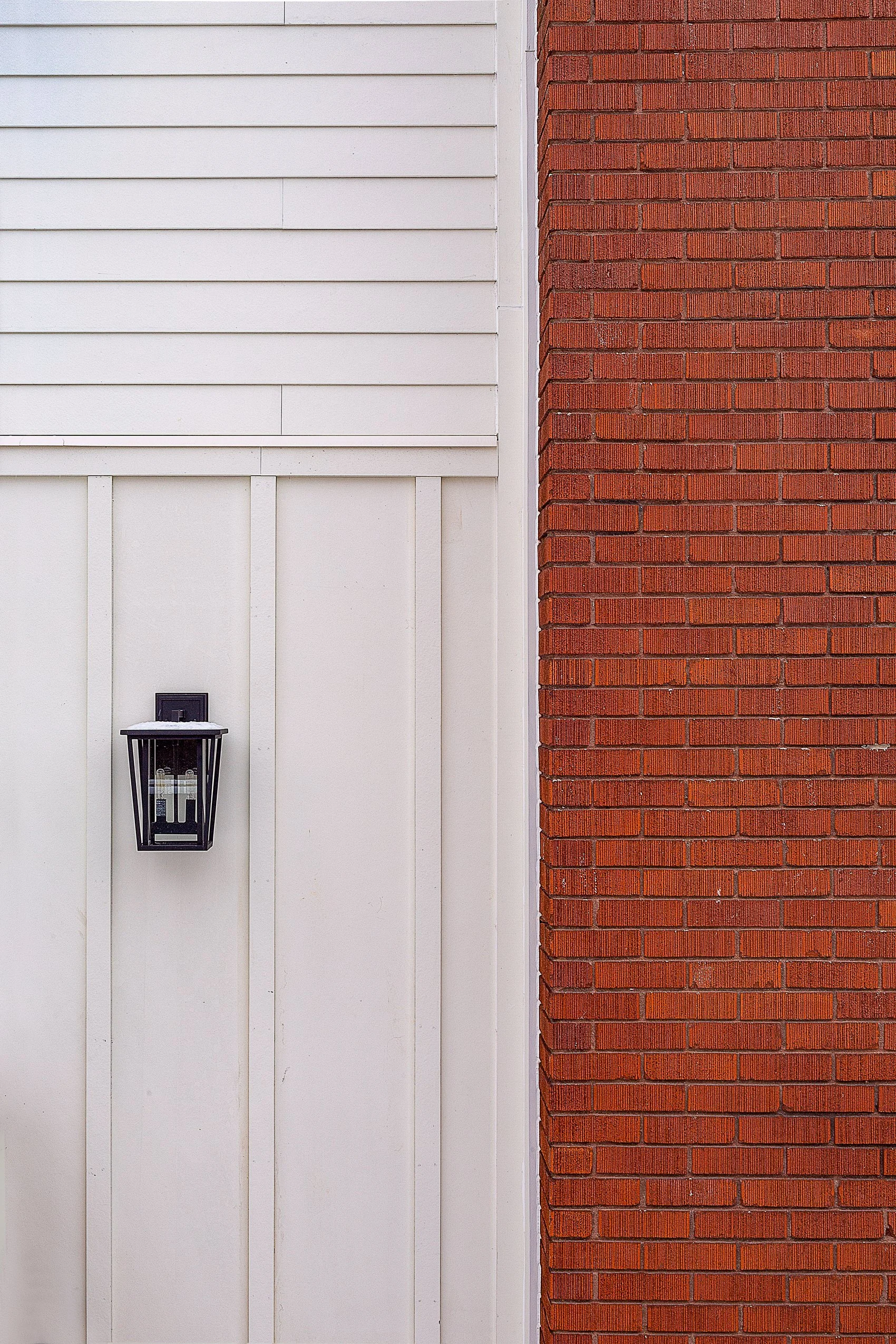 Close-up of a white wall with horizontal siding, a red brick wall, and a black outdoor lantern.