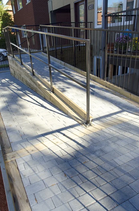 Construction site with a metal wheelchair ramp and brick-paved walkway outside a residential building.