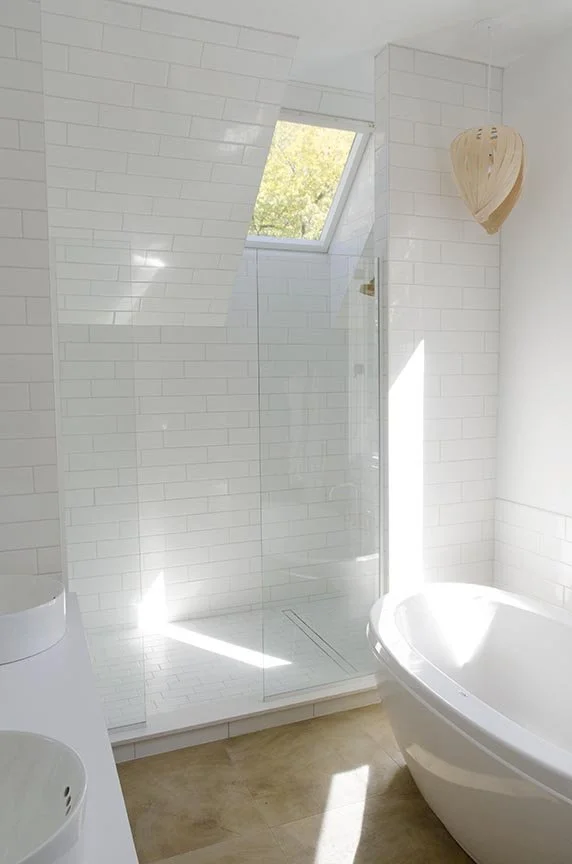 Modern bathroom with a glass shower enclosure, a skylight, a white bathtub, and white subway tile walls.