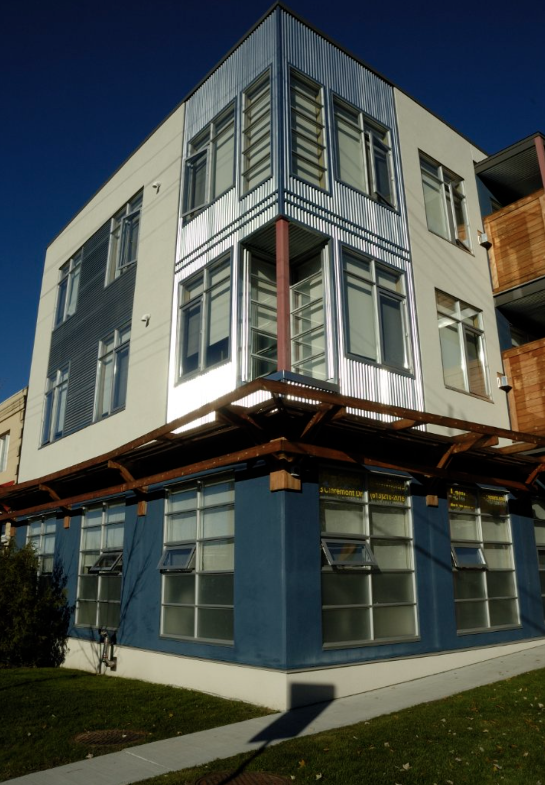 A multi-story modern building with metal and glass exterior, featuring large windows, some open, under a clear dark blue sky.