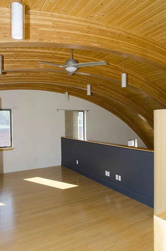 Mezzanine with a curved wooden ceiling, ceiling fan, pendant lights, two windows, and a half wall painted dark blue.