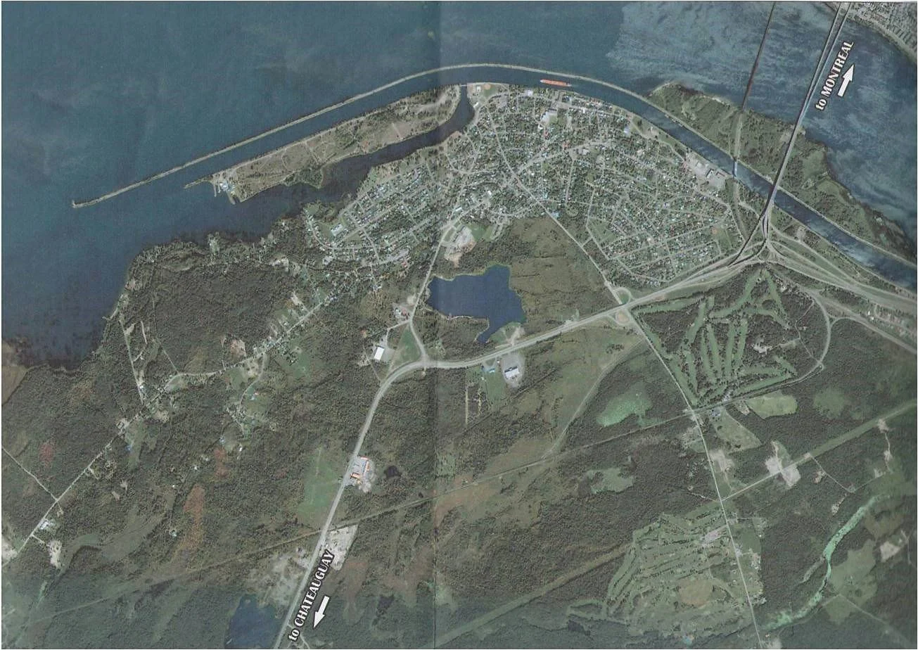 Satellite map showing a town near a river with roads, residential areas, a lake, and surrounding greenery. The map includes labels indicating directions to Montreal and Chute-A-Gamy.