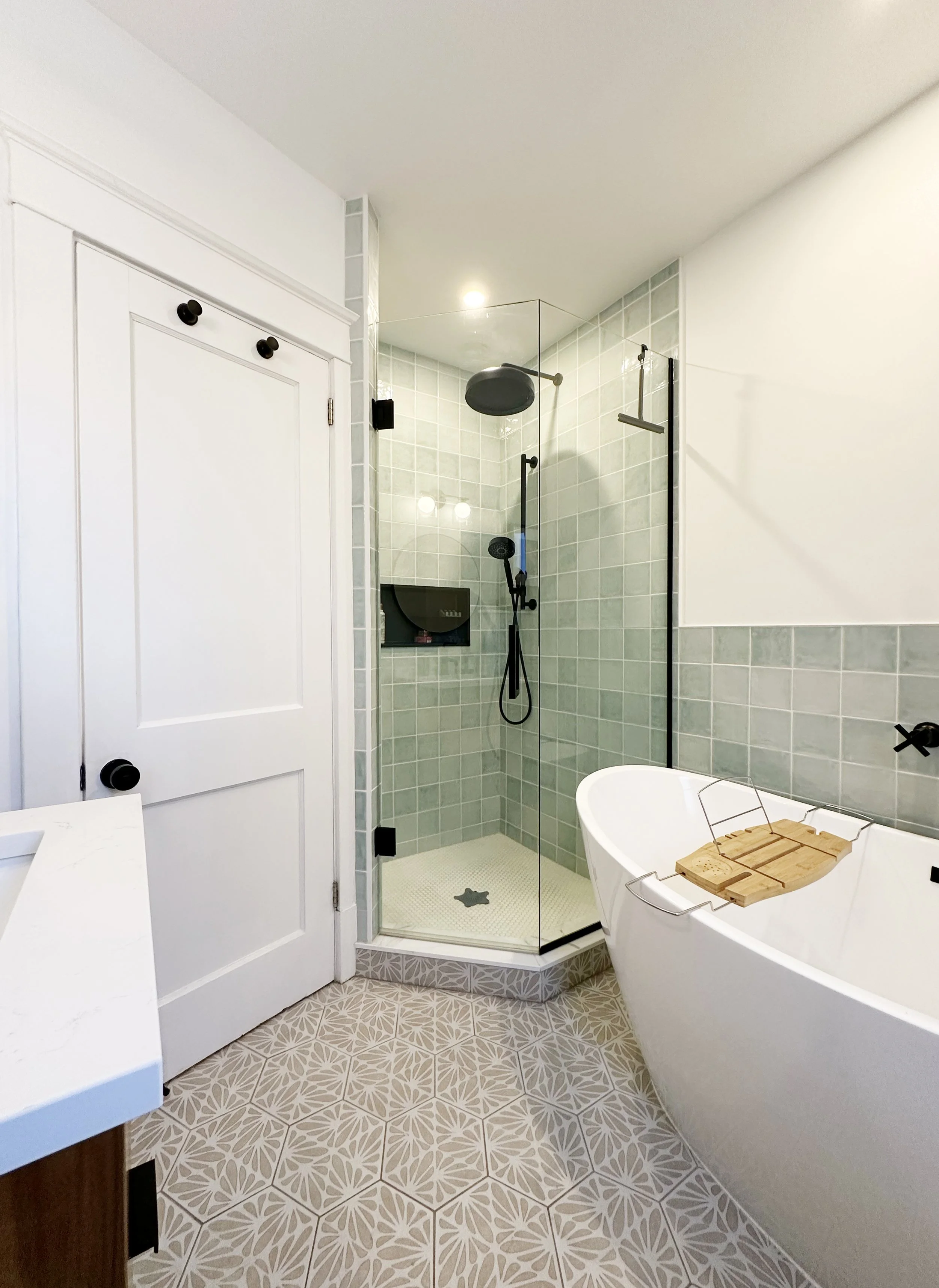 A spa bathroom with a walk-in shower, a white bathtub with a wooden bath tray, and patterned tile flooring.