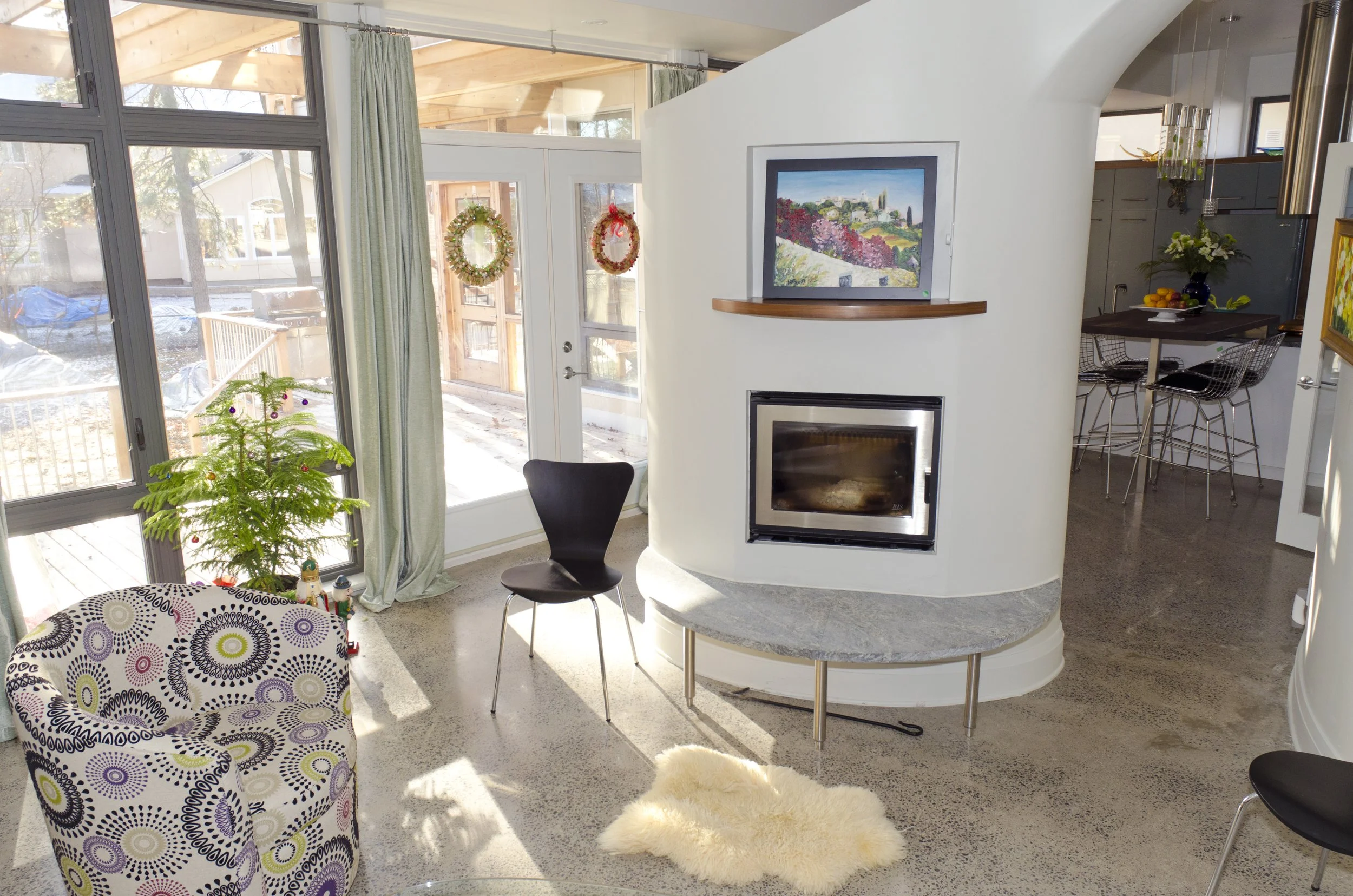 Living room with a modern fireplace, TV above, decorated for Christmas, large windows, and a small Christmas tree.