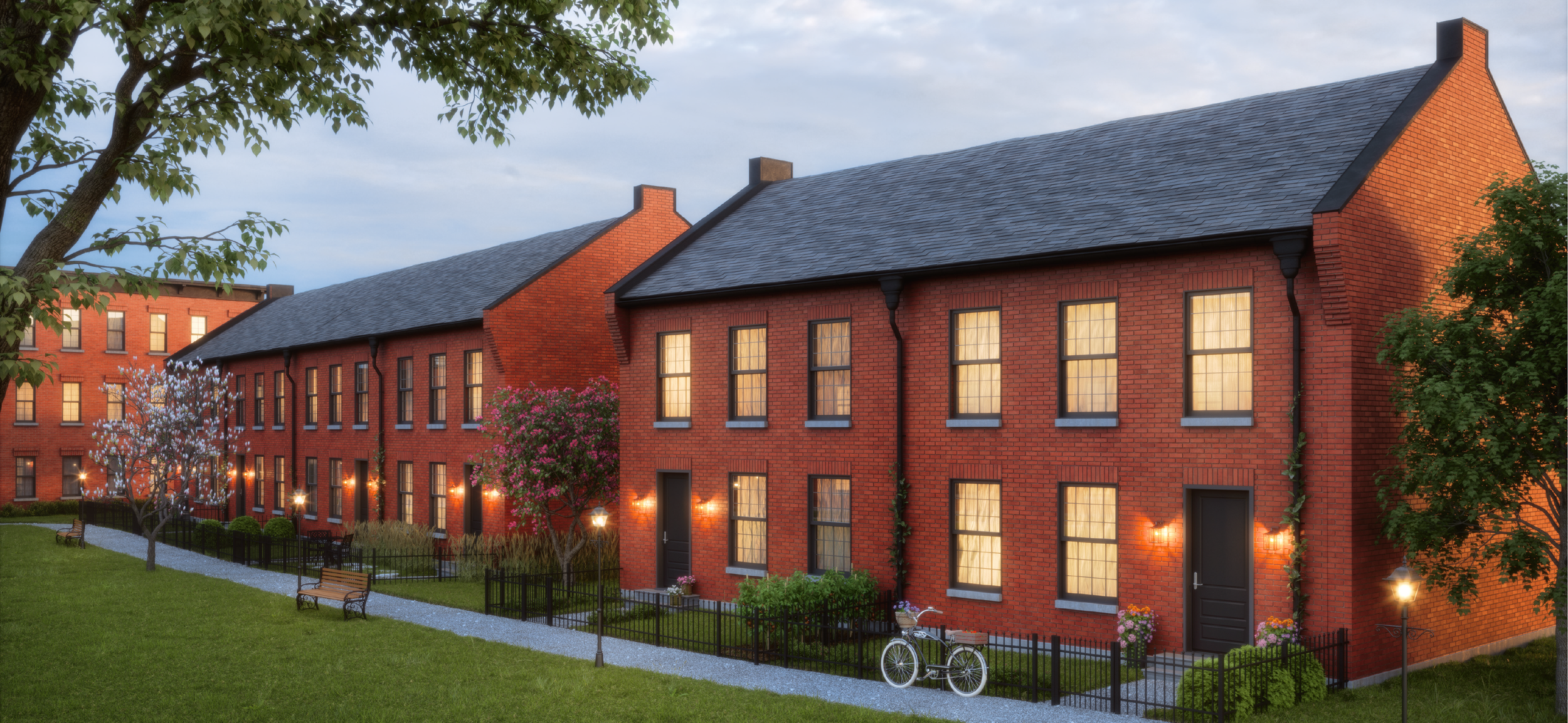 View of red brick apartment buildings at dusk with lit windows, trees, a bike, and a walking path.