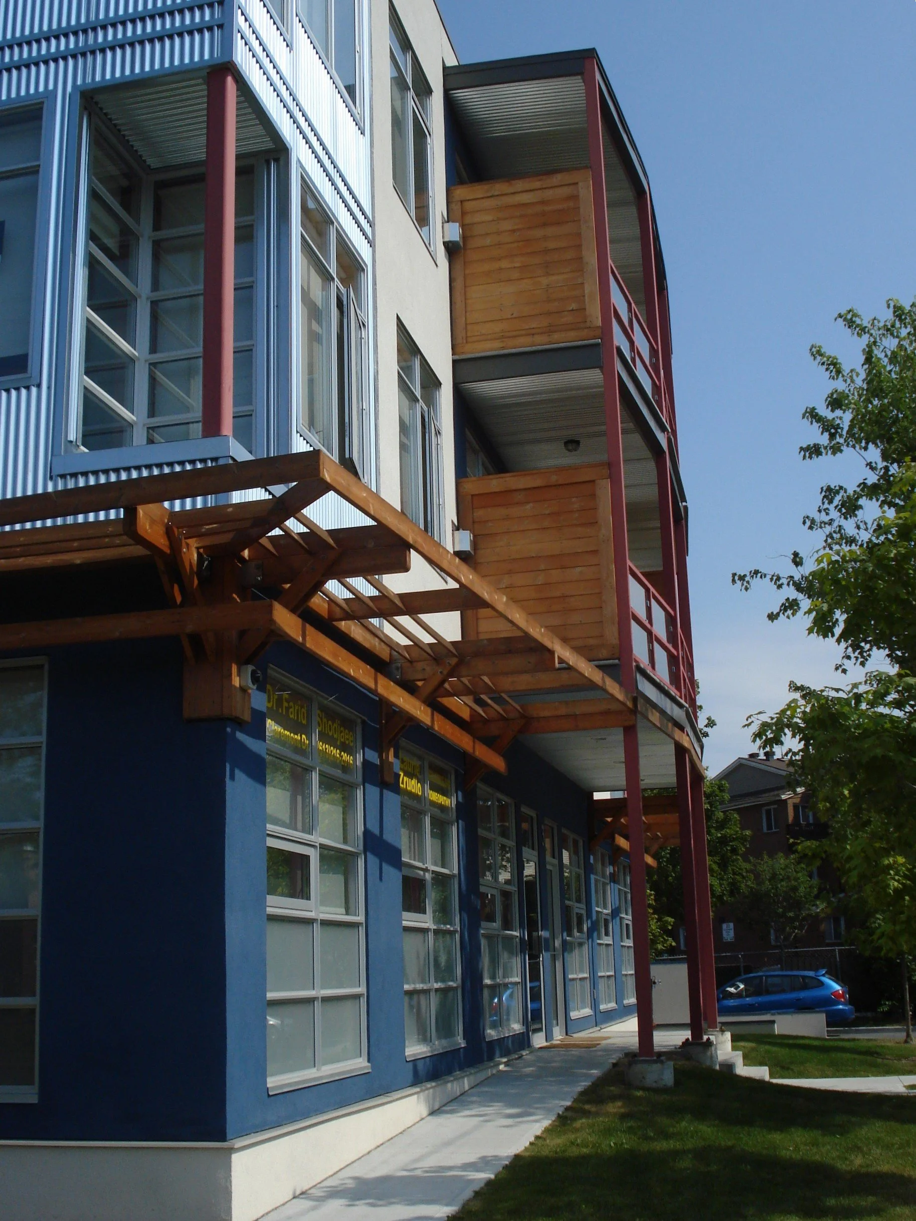Modern multi-story building with a blue ground floor, large windows, and wooden balconies on the upper floors, with some construction or renovation work ongoing.
