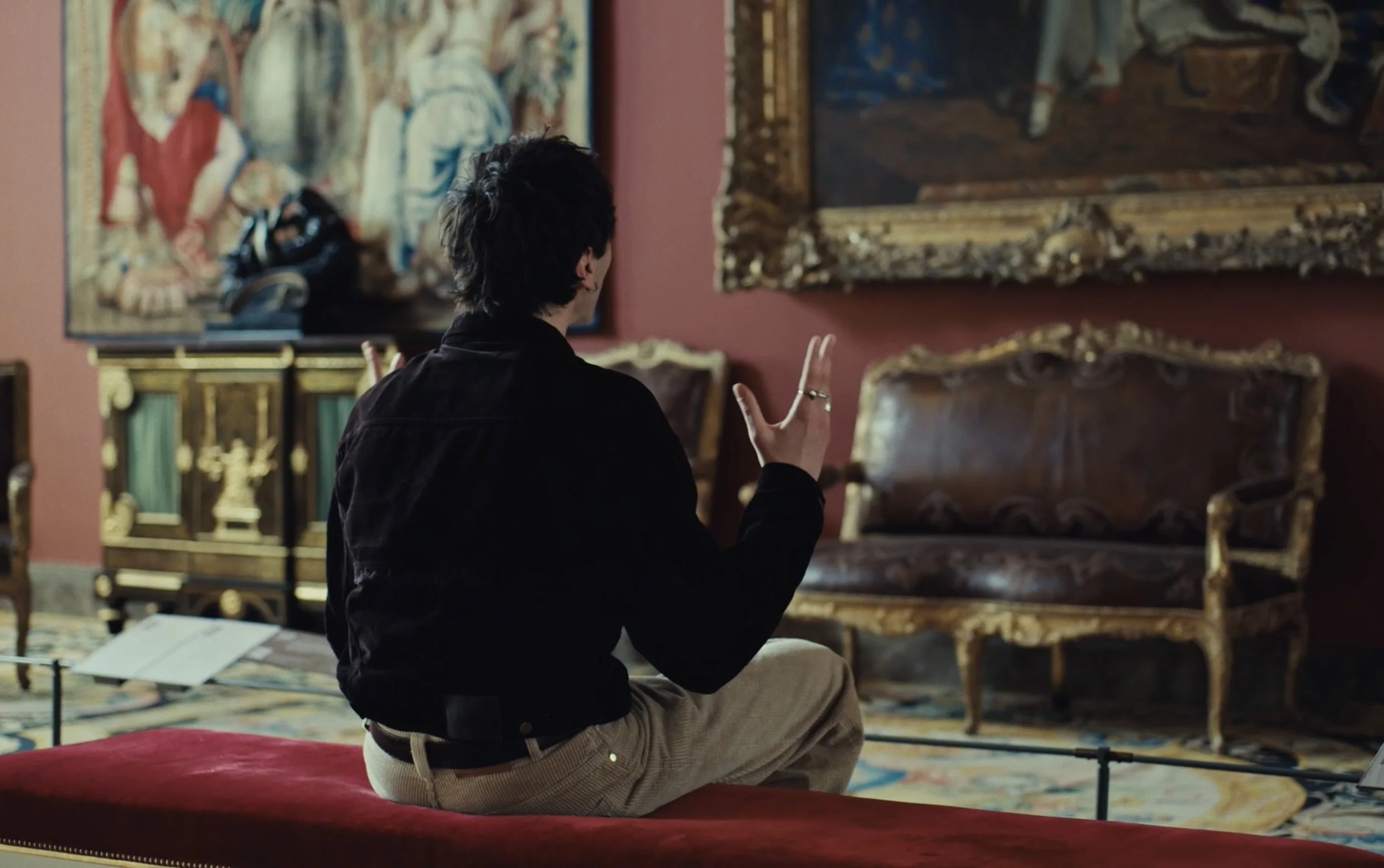Une personne assise sur un banc, vue de dos, devant des tableaux artistiques dans un musée