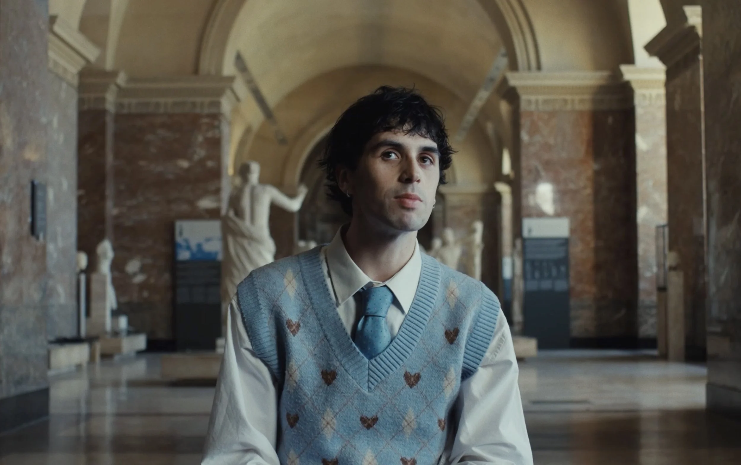 Un jeune homme assis dans un musée avec des statues en marbre en arrière-plan.