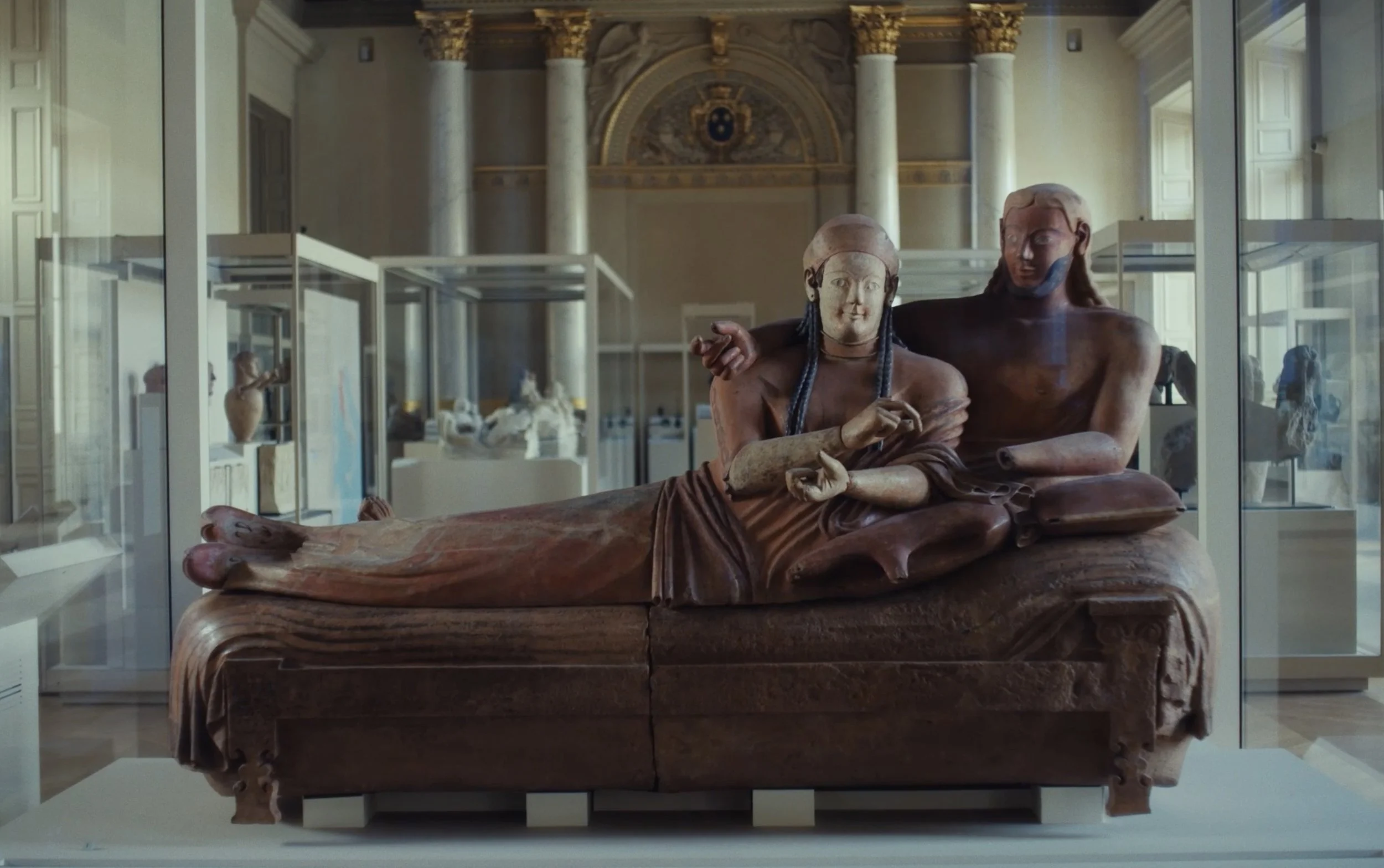 Une sculpture ancienne représentant une scène de repos avec deux figures, dont une femme allongée et un homme assis, exposée dans un musée.