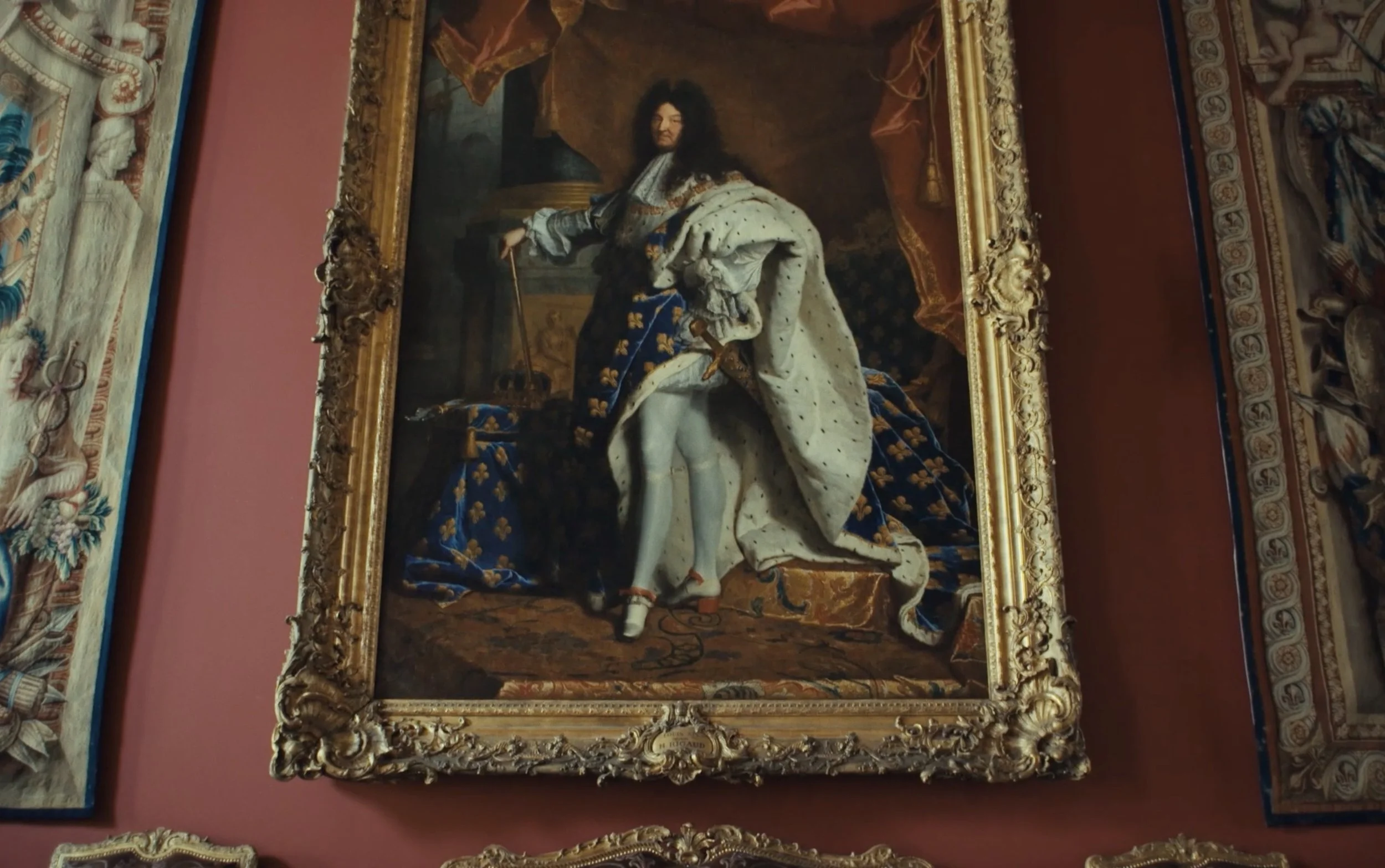 Un tableau représentant un roi en tenue royale avec une cape et un sceptre, assis et debout devant un fond sombre dans un cadre doré ornée de tissus somptueux.