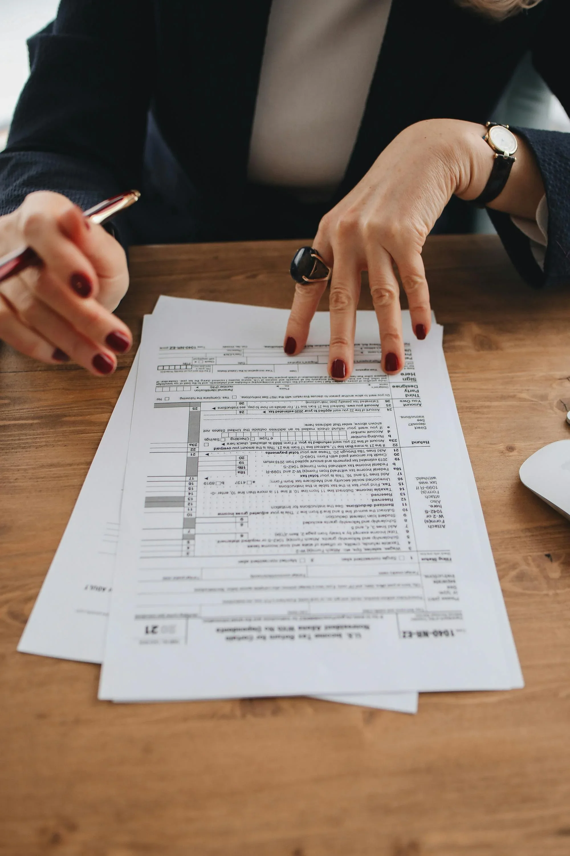 A person reviewing a printed tax form at a wooden desk.