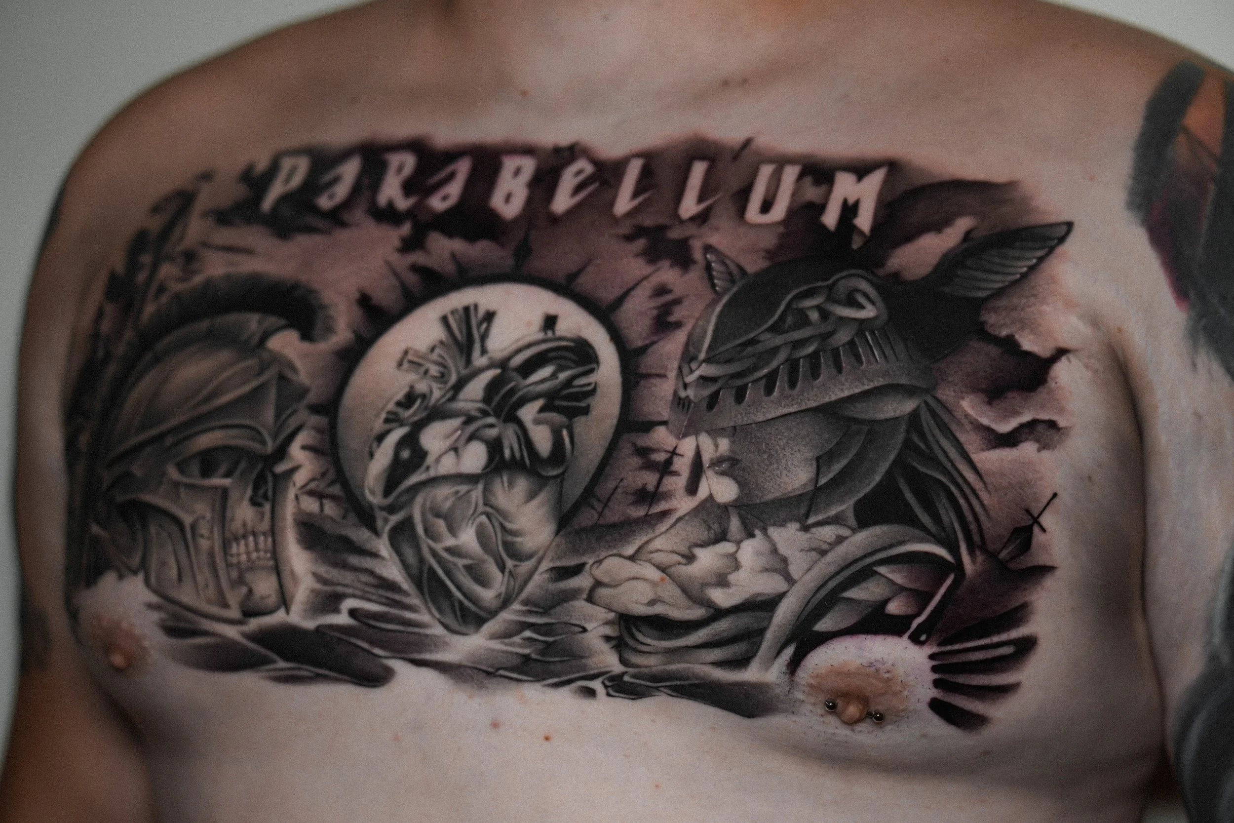 Chest tattoo featuring a Roman-style helmet, anatomical heart, and warrior with the word 'PARABELLUM'.