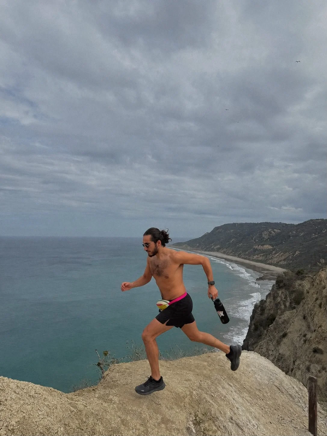 José Alejandro López Díaz running on rocks, with a coastal view behind him.