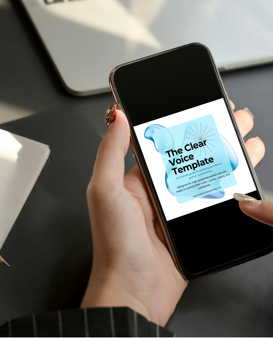 Smartphone screen showing ‘The Clear Voice Template’ by Maggie Franco, held in one hand above a dark desk with a laptop in the background.