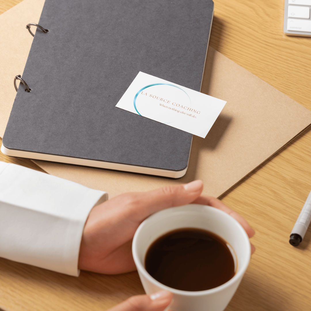 A La Source Coaching business card resting on a notebook with a cup of coffee, symbolizing calm, clarity, and the supportive approach of Emotional Intelligence Coach Maggie Franco.