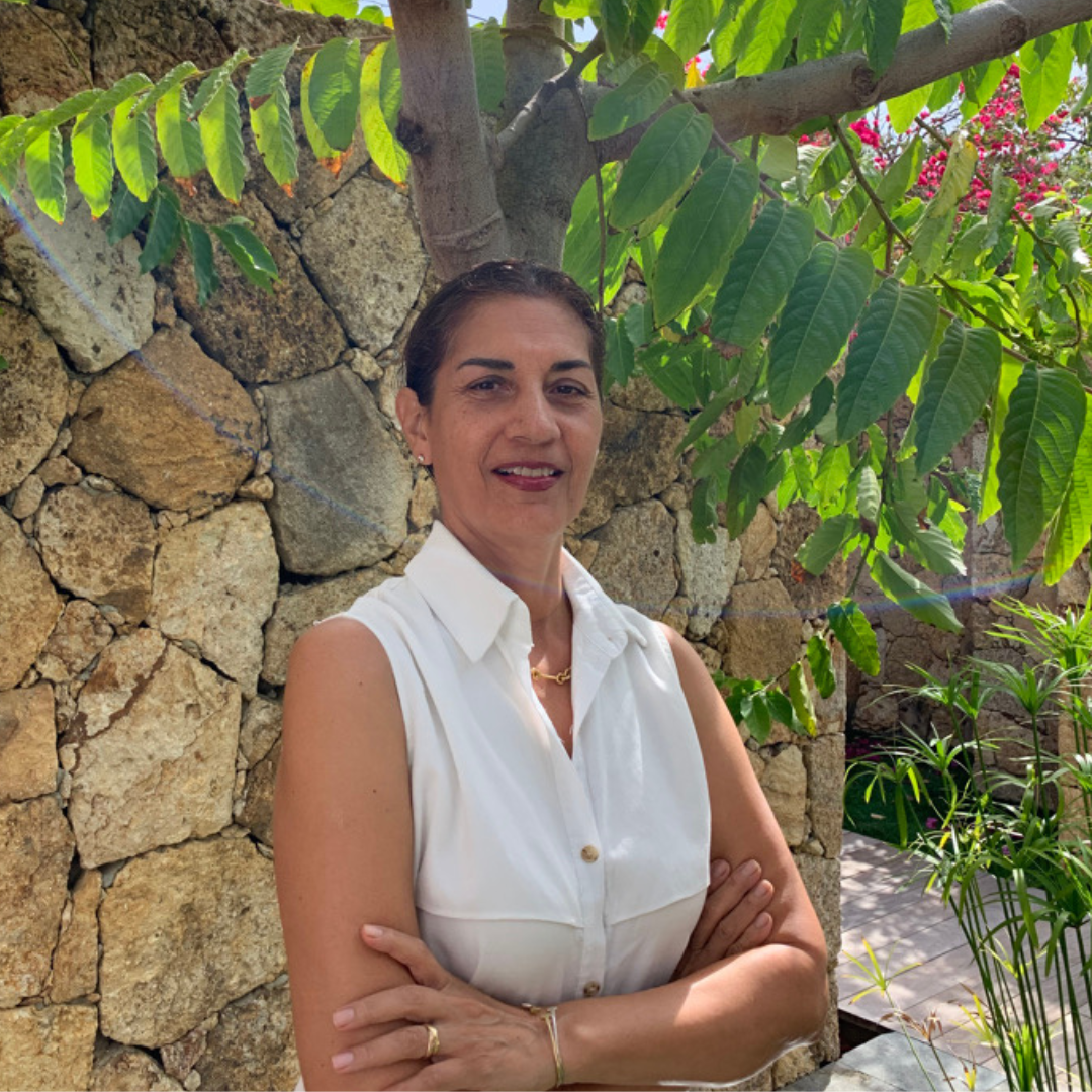 Maggie Franco, Emotional Intelligence and Leadership Coach, standing outdoors in natural light with a stone wall and lush greenery behind her, smiling with calm confidence.