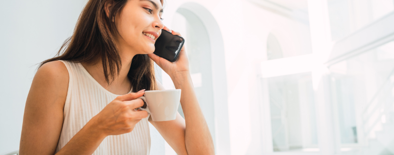 Smiling woman talking on the phone with a coffee cup in a bright room.