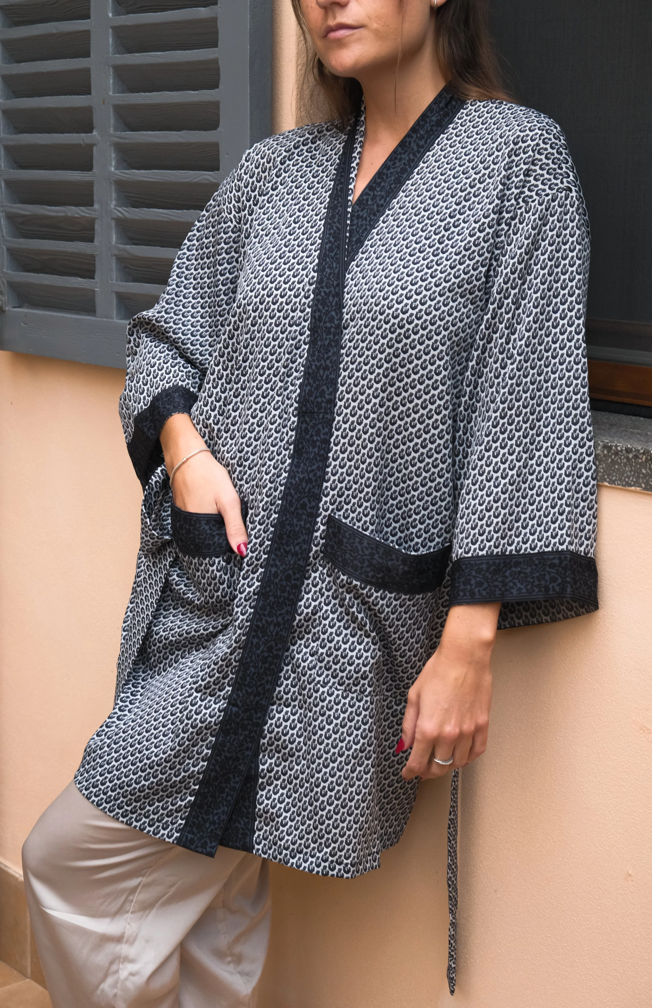 Mujer vistiendo un kimono gris con estampado negro de pie junto a una pared, con la mano en el bolsillo.