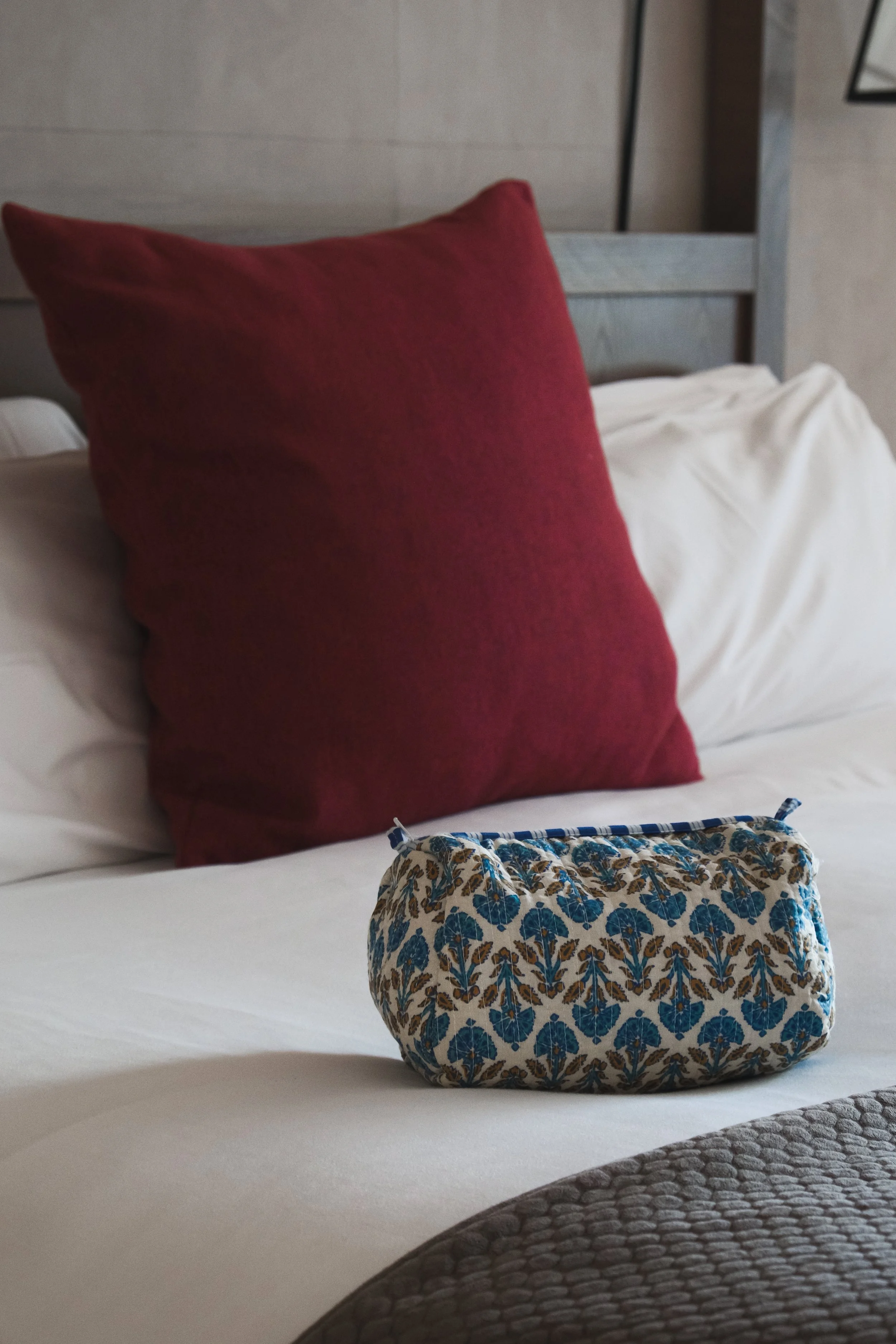 Cojín rojo en una cama blanca con una bolsa estampada frente a él.