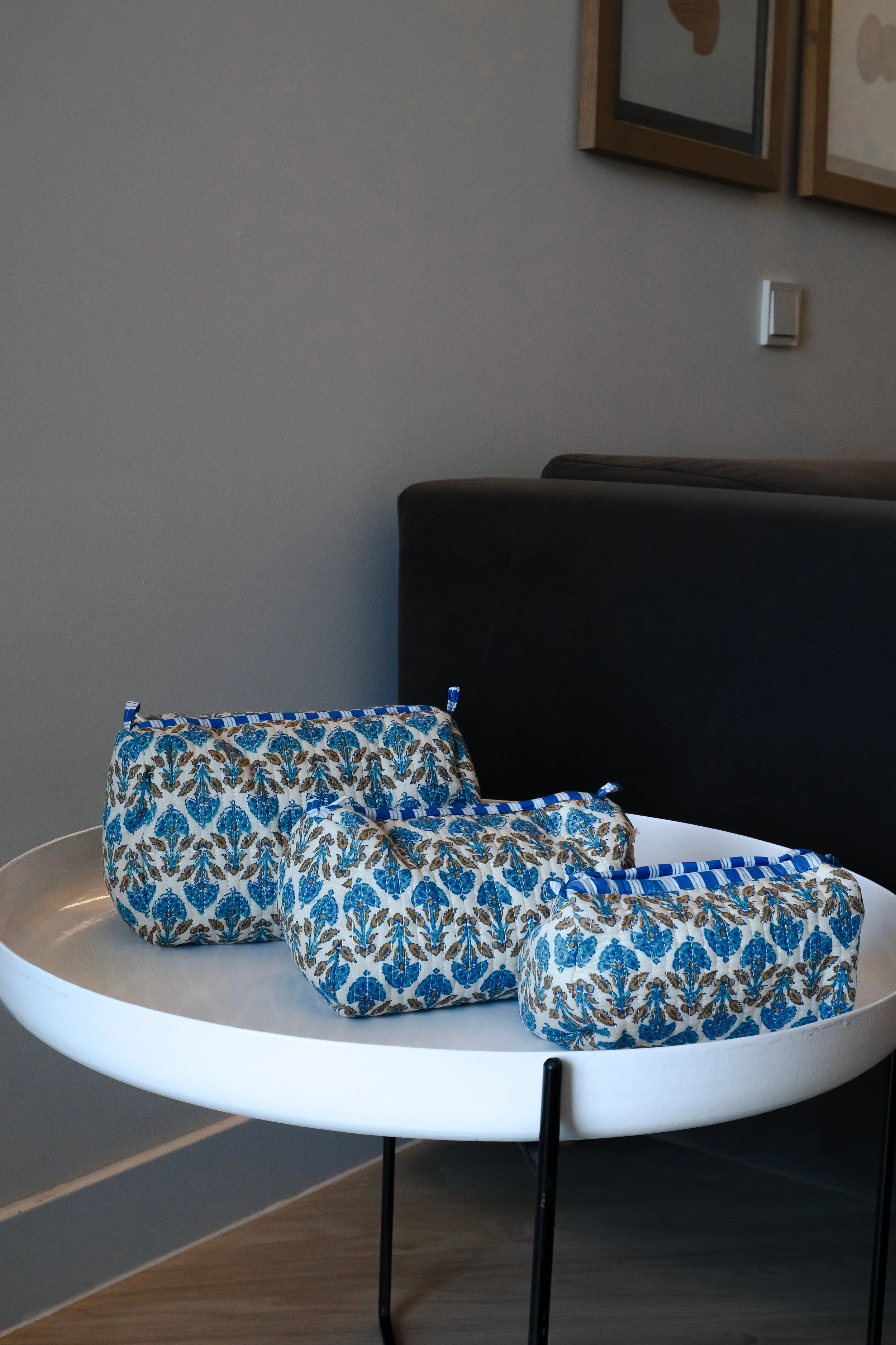 Tres bolsas de tela con estampado azul y blanco sobre una mesa redonda blanca, frente a un sofá oscuro.