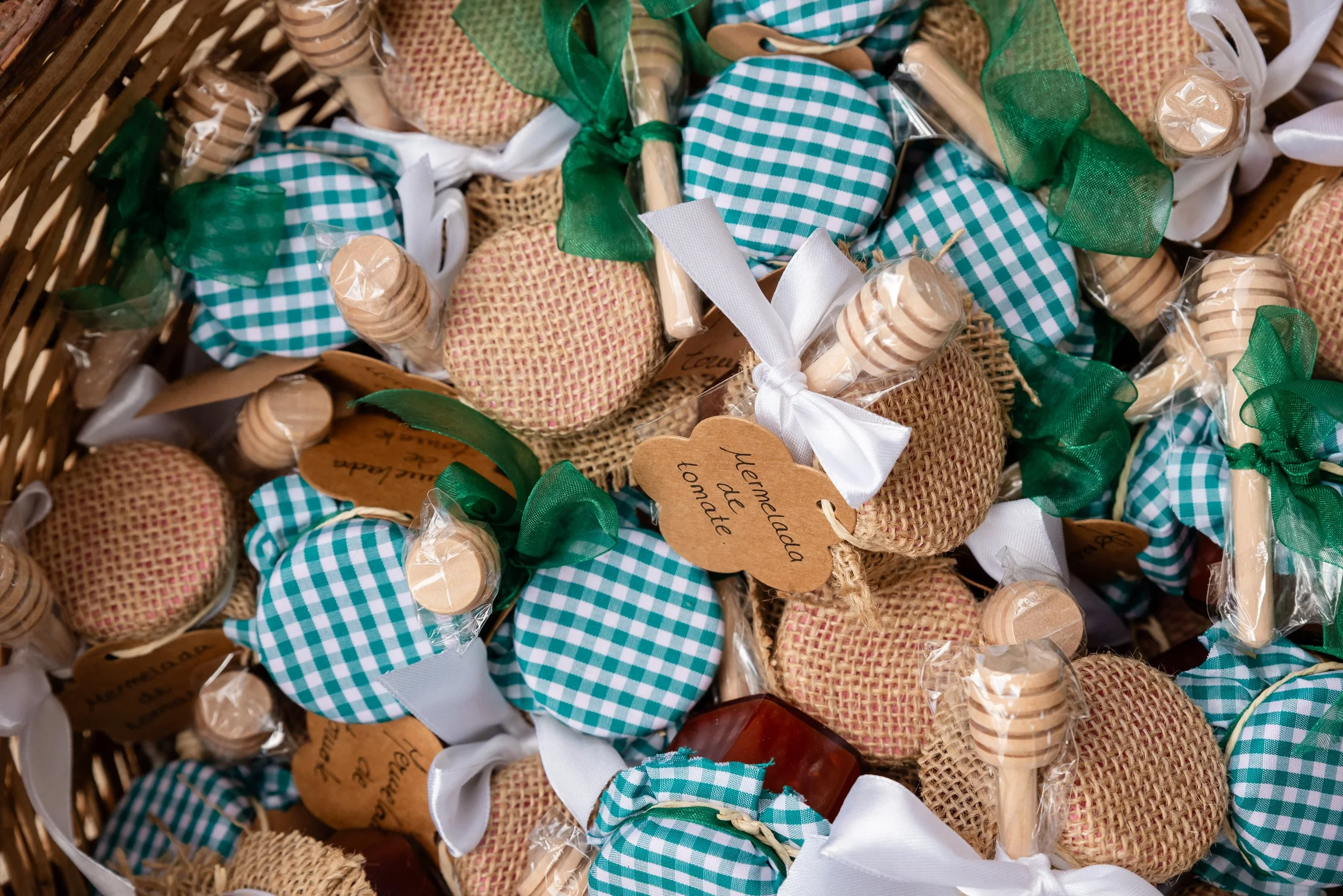 Tarros de mermelada decorados con telas de cuadros verdes y naturales, con lazos y cucharas de madera, en una canasta.