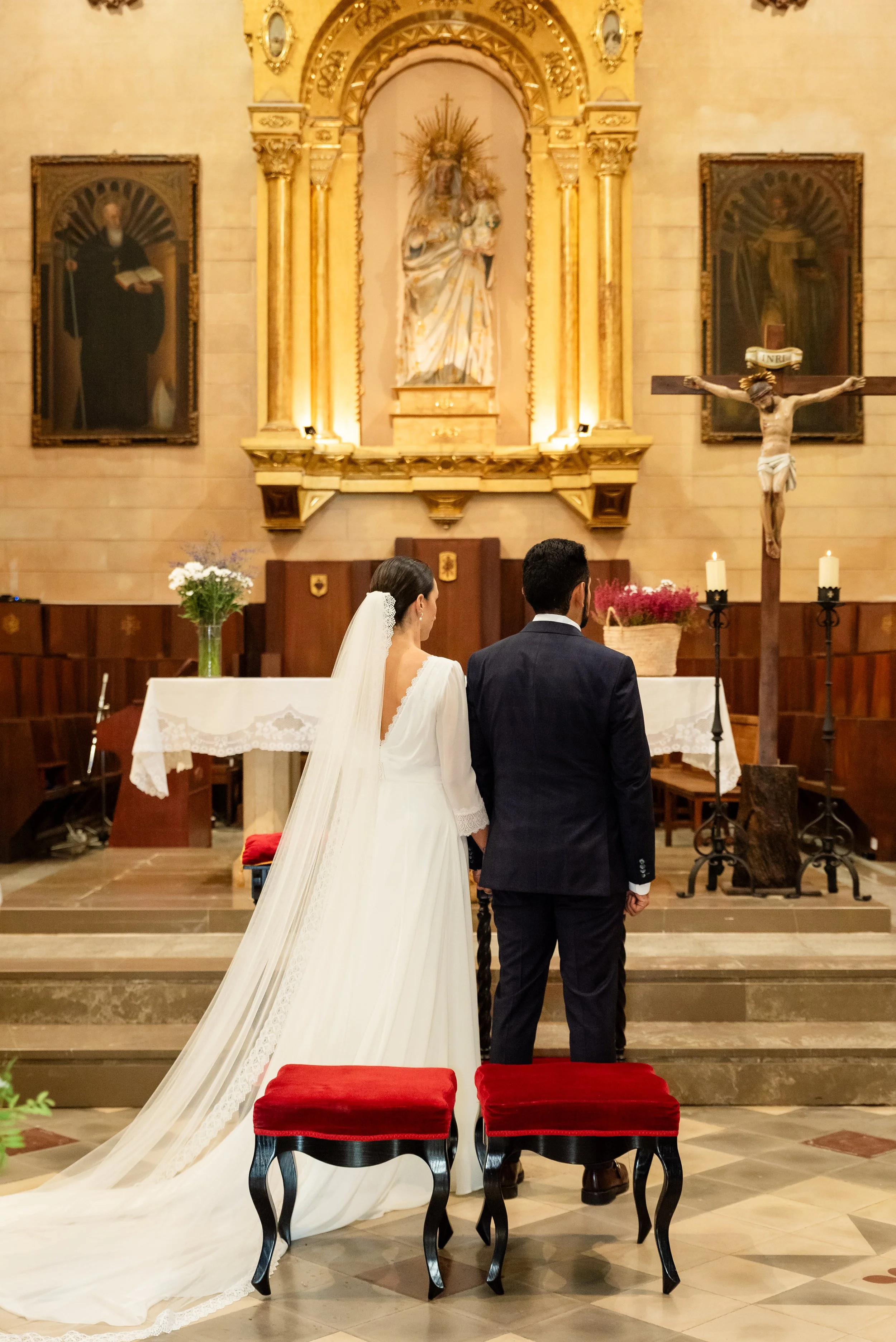 Pareja en ceremonia de boda en una iglesia, de pie ante el altar, con imágenes religiosas y un crucifijo.