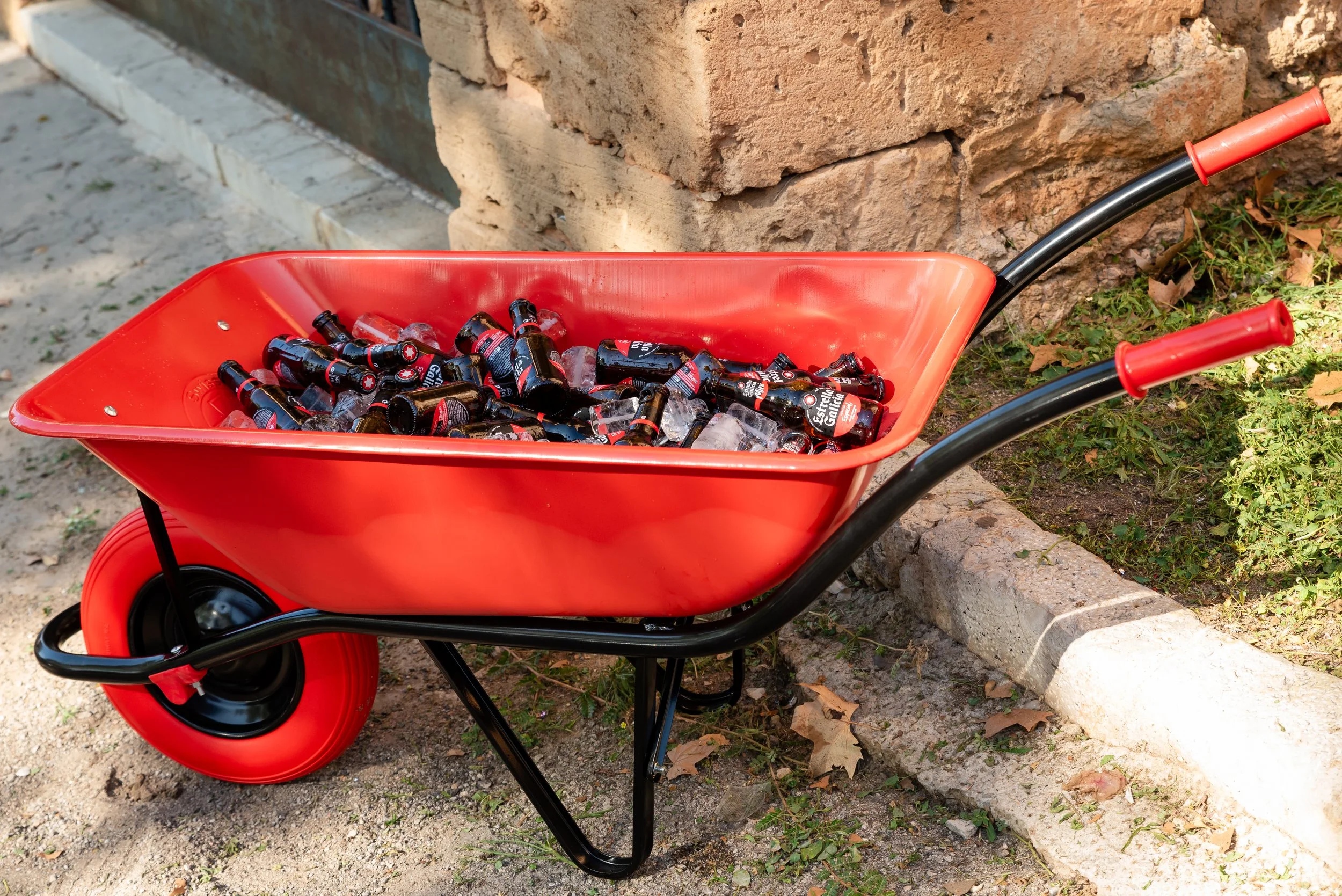 Carretilla roja con botellas de cerveza y hielo al aire libre.