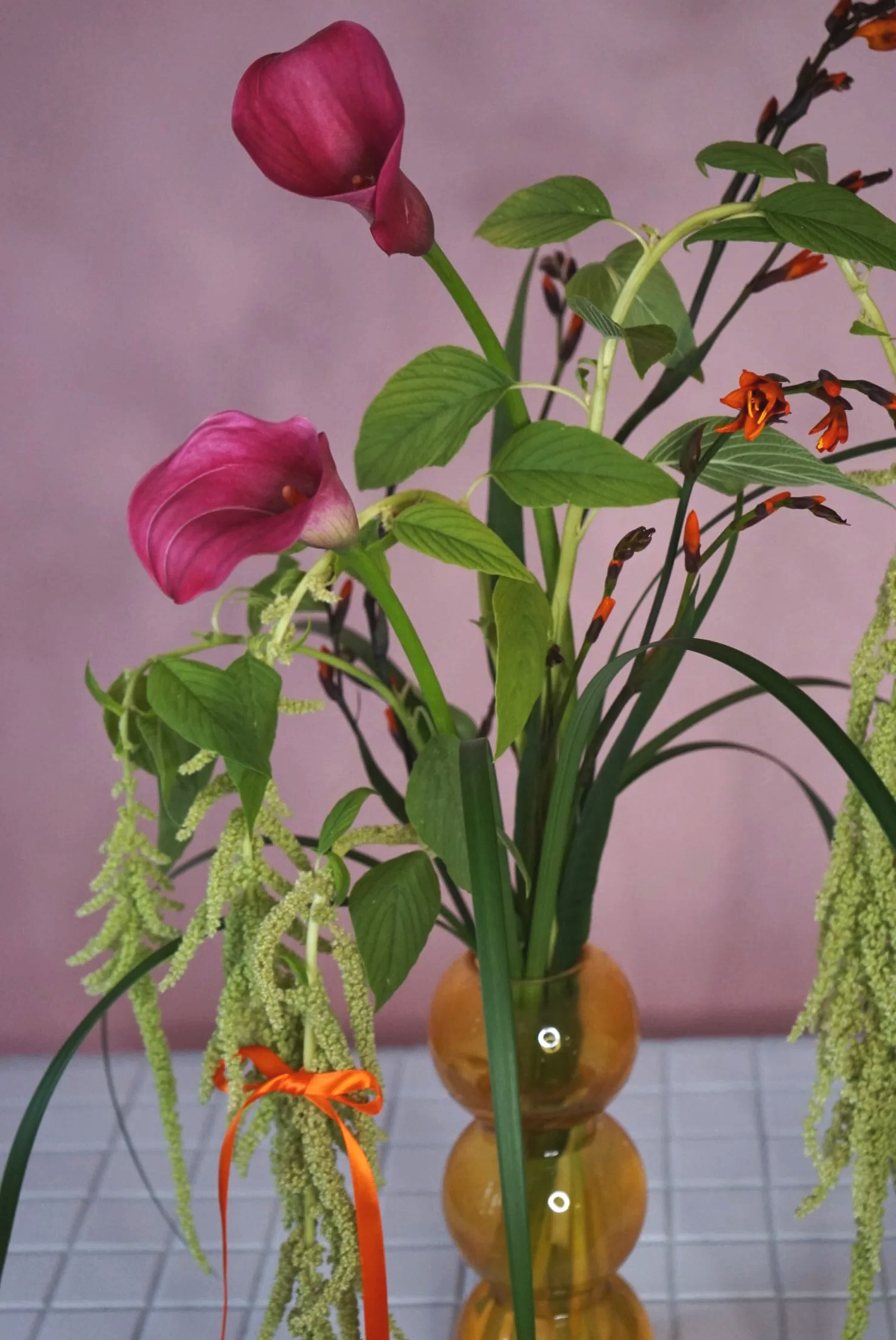 Kukka-asetelma persoonallisilla kukilla ja rusetilla asetettuna maljakkoon.