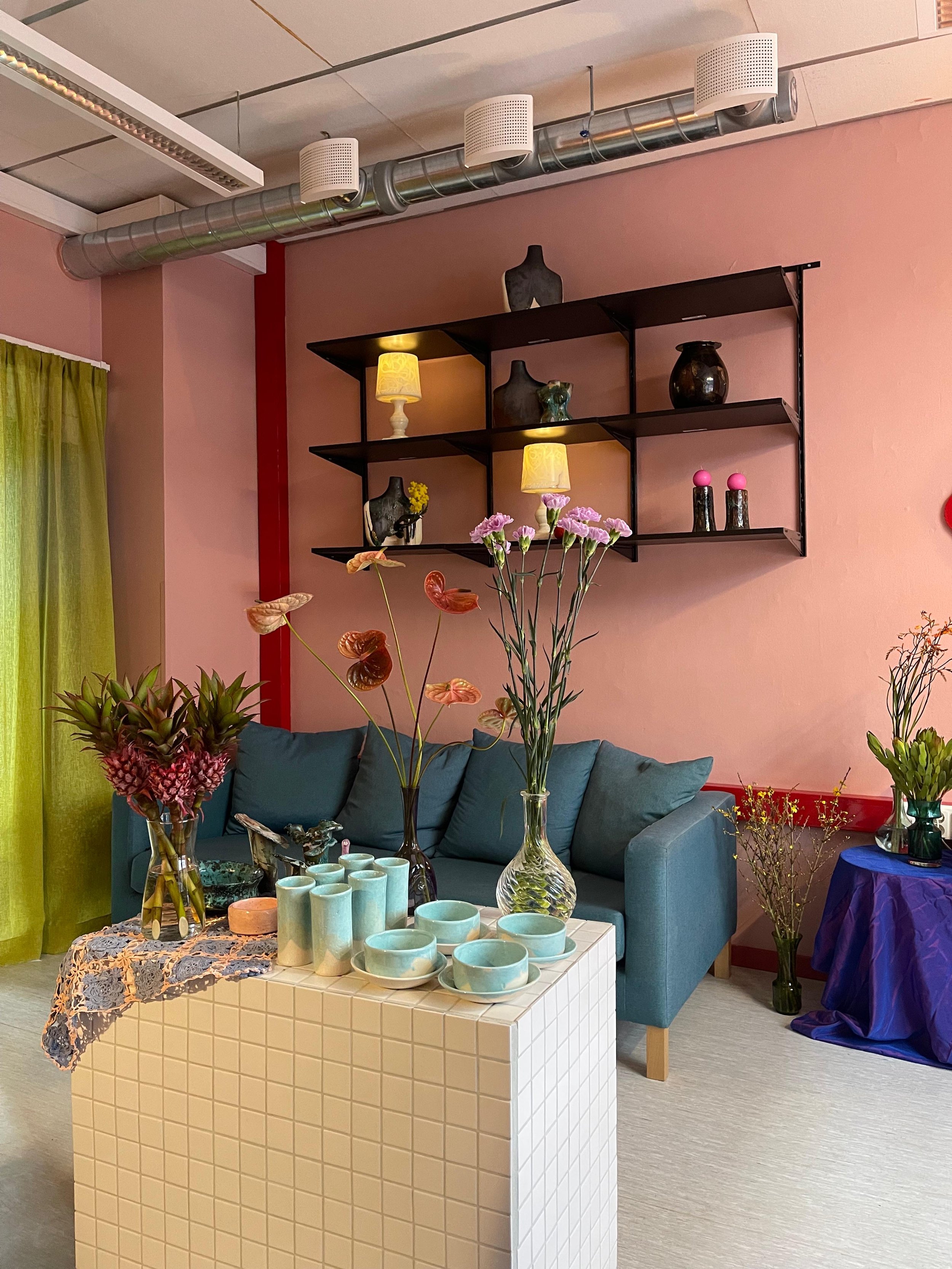 Heben myymälä, jossa on sininen sohva ja kukkia. Seinällä on hyllykkö, jossa on koriste-esineitä ja pieniä lamppuja.