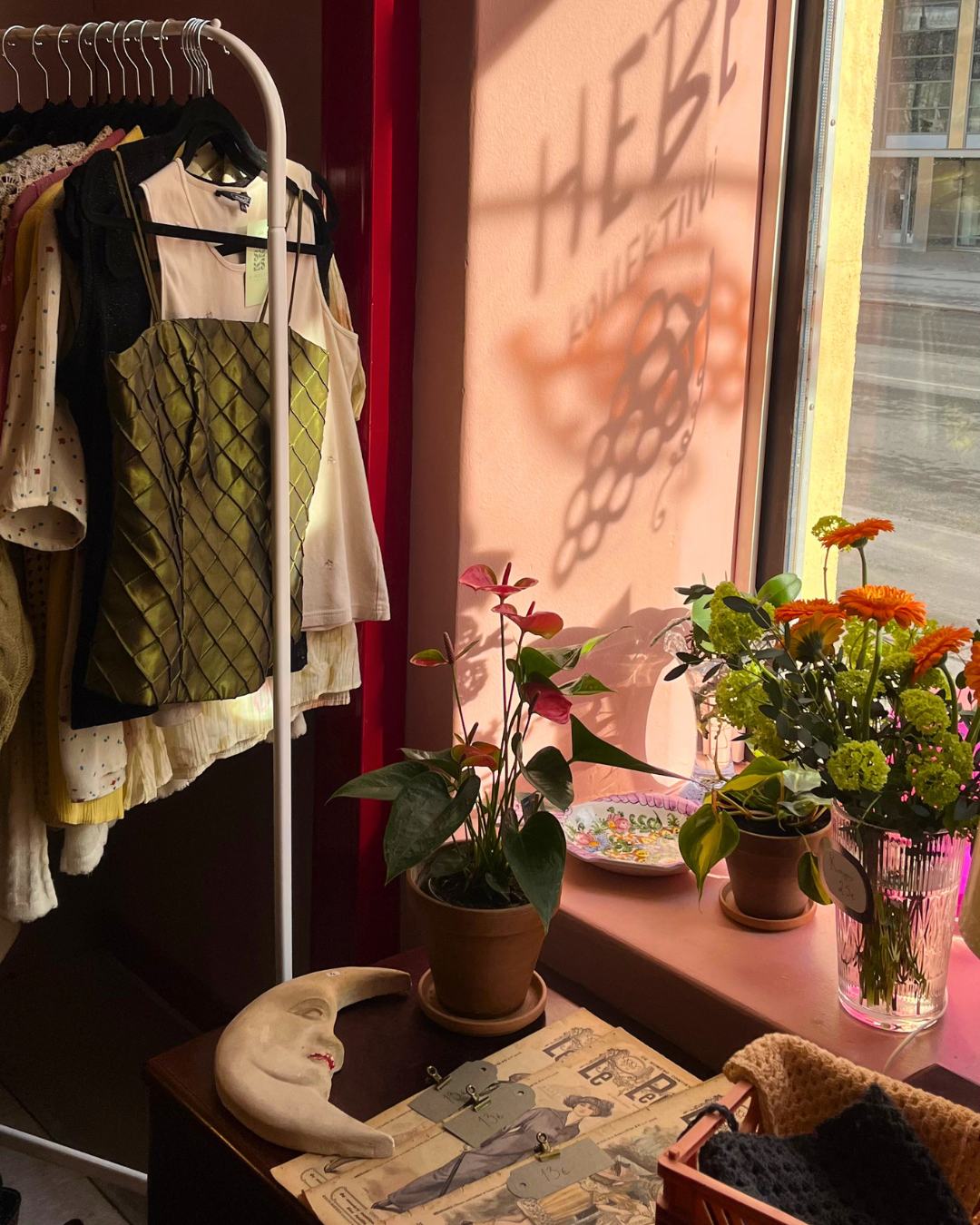 Pop-up vintagemyymälän esillepano, jossa vaatteita rekissä, vanha kuuseinäkoriste ja ranskalaisia lehtiä pöydällä.