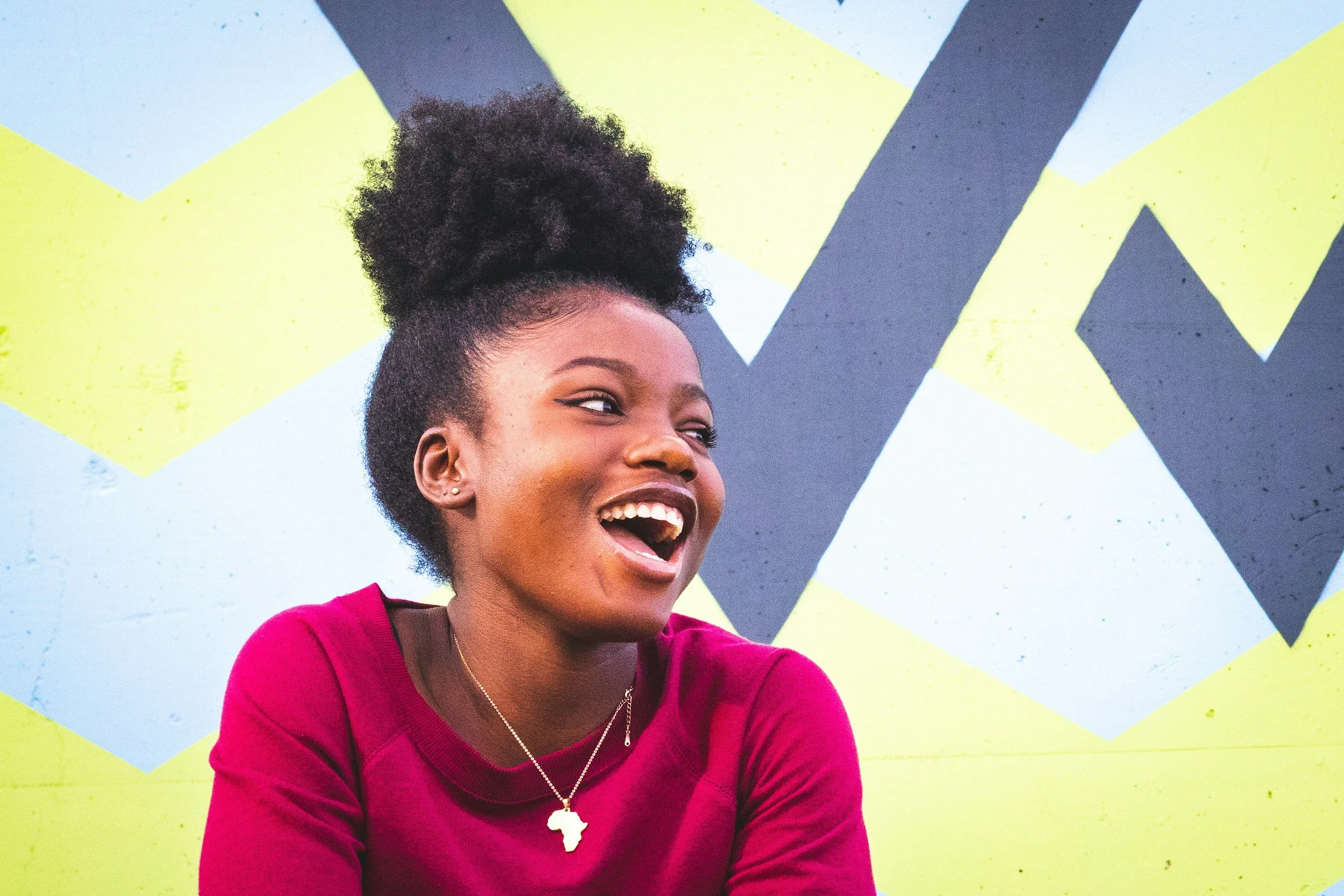 Smiling woman with curly hair in front of colorful zigzag mural.