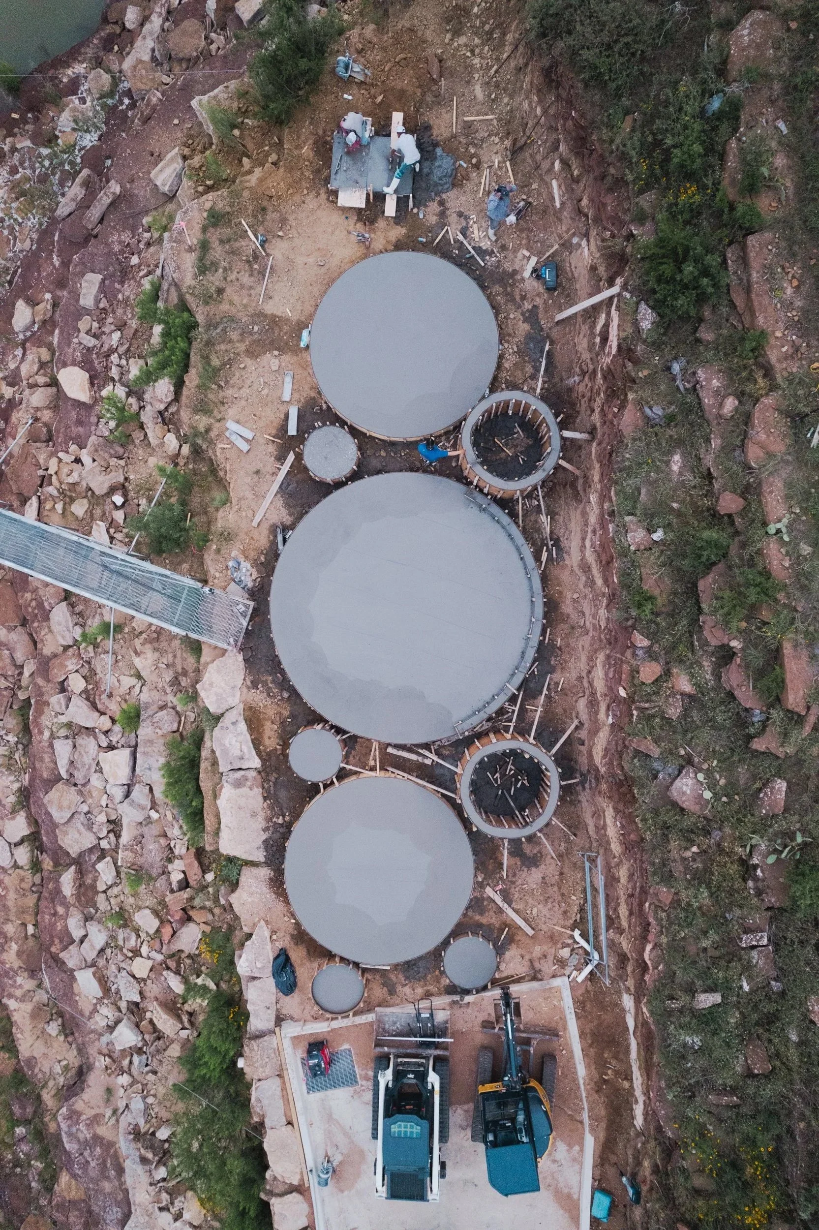 Aerial view of circular concrete structures under construction on a rocky hillside.